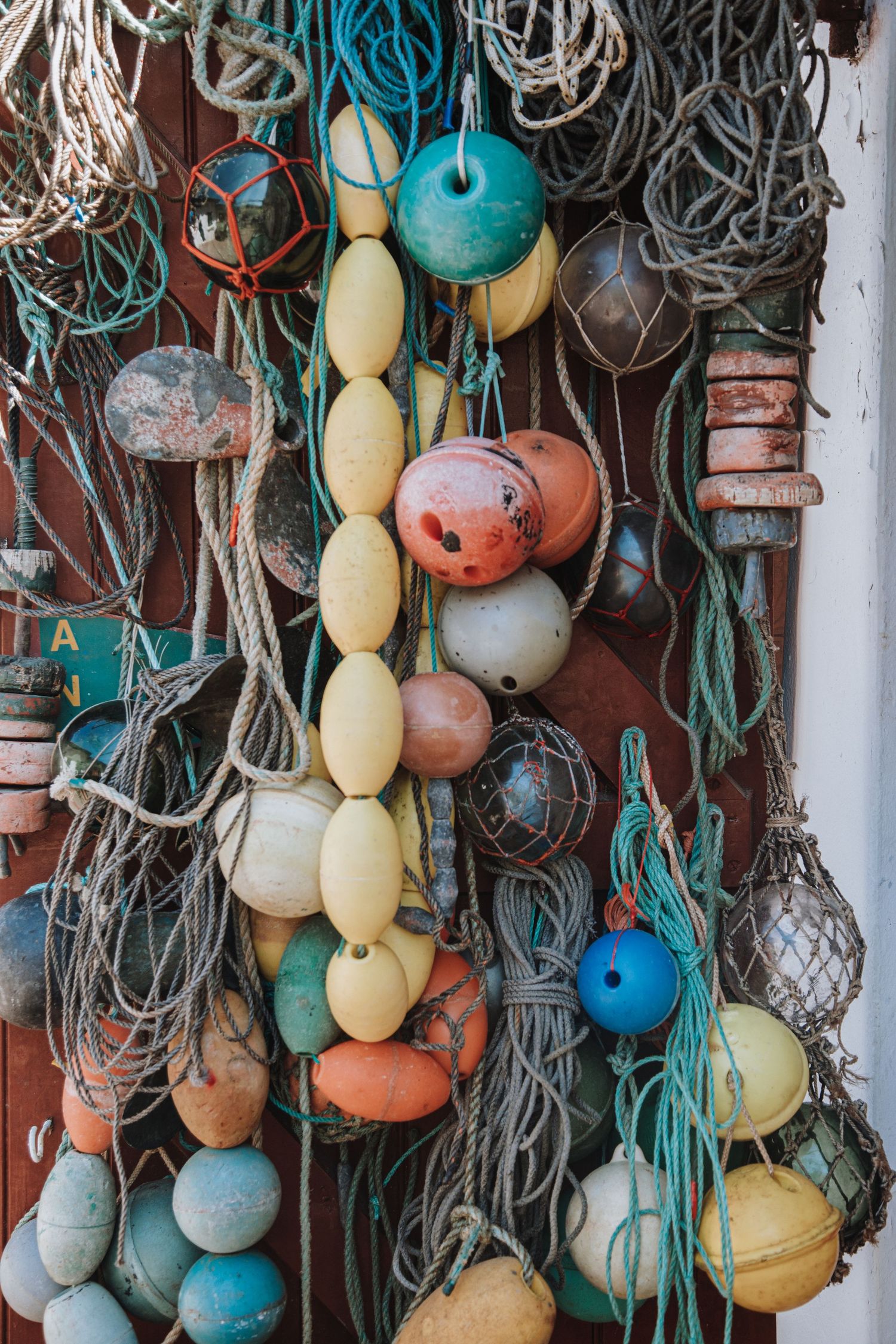 Colorful vintage fishing buoys and floats in turquoise, orange, and yellow hanging against weathered wood with rope netting.