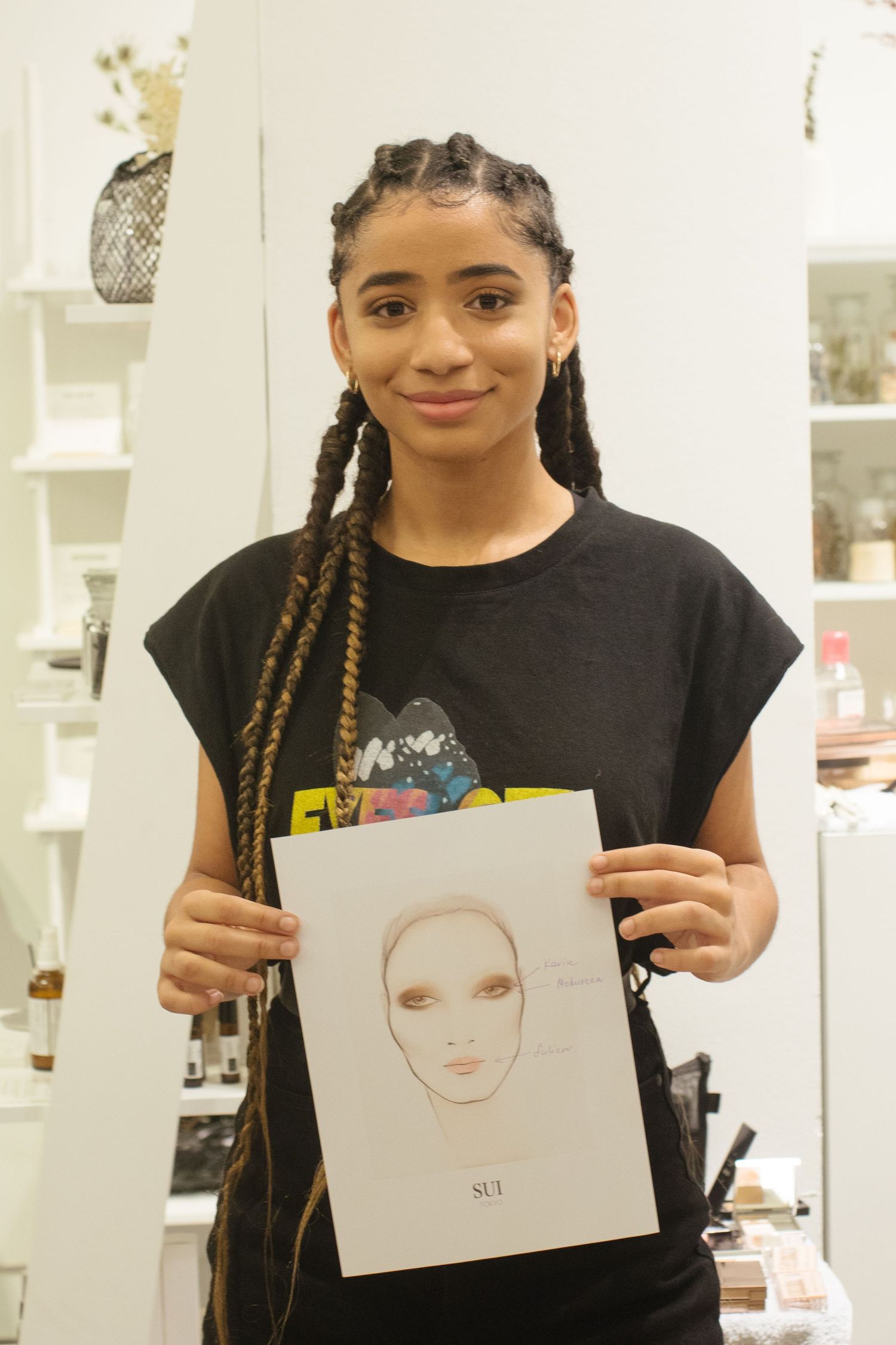 A student in a black t-shirt holds up their artwork showing a portrait sketch during an art class.