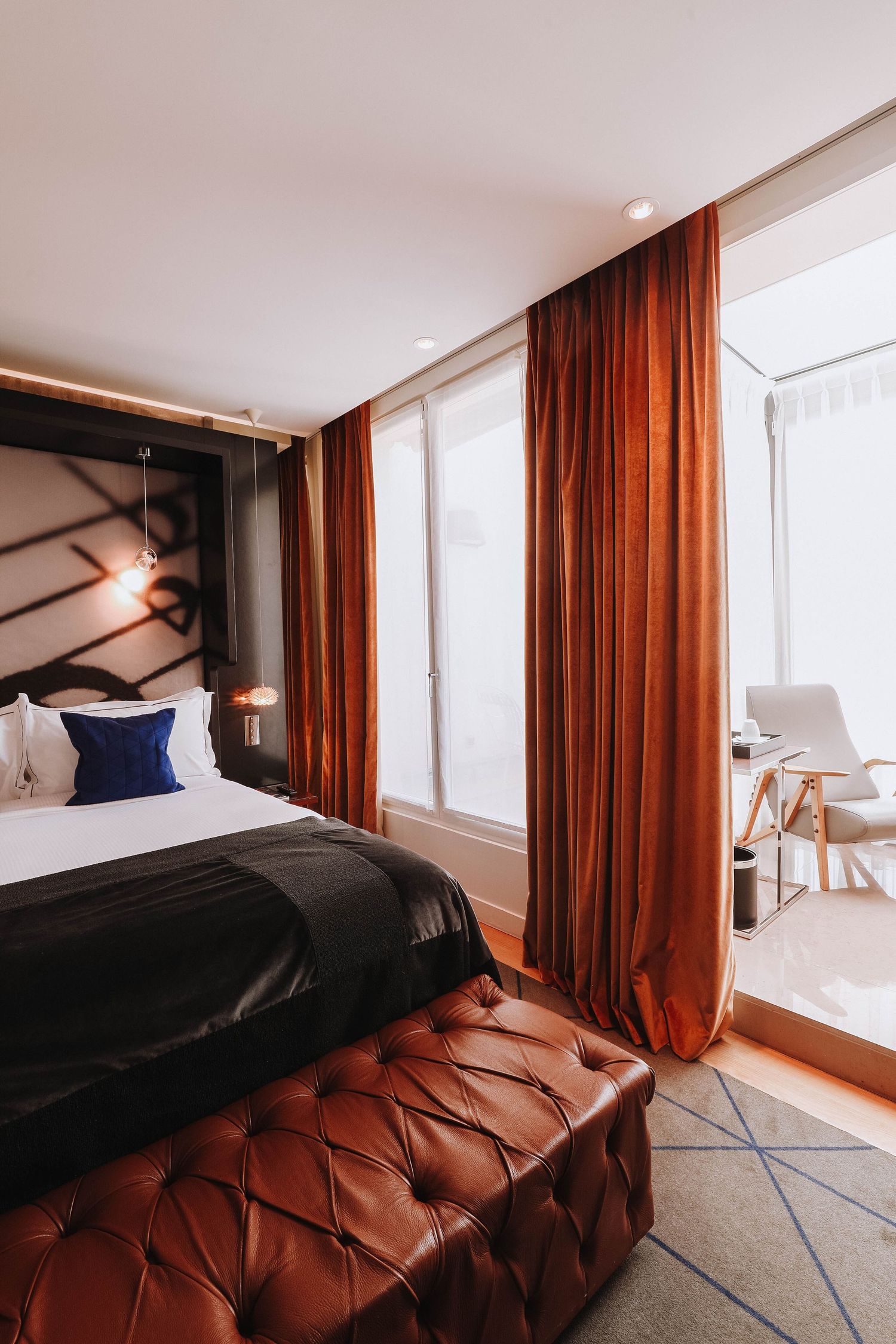 Modern bedroom interior with rustic brown curtains and tufted leather headboard against white walls and natural lighting.