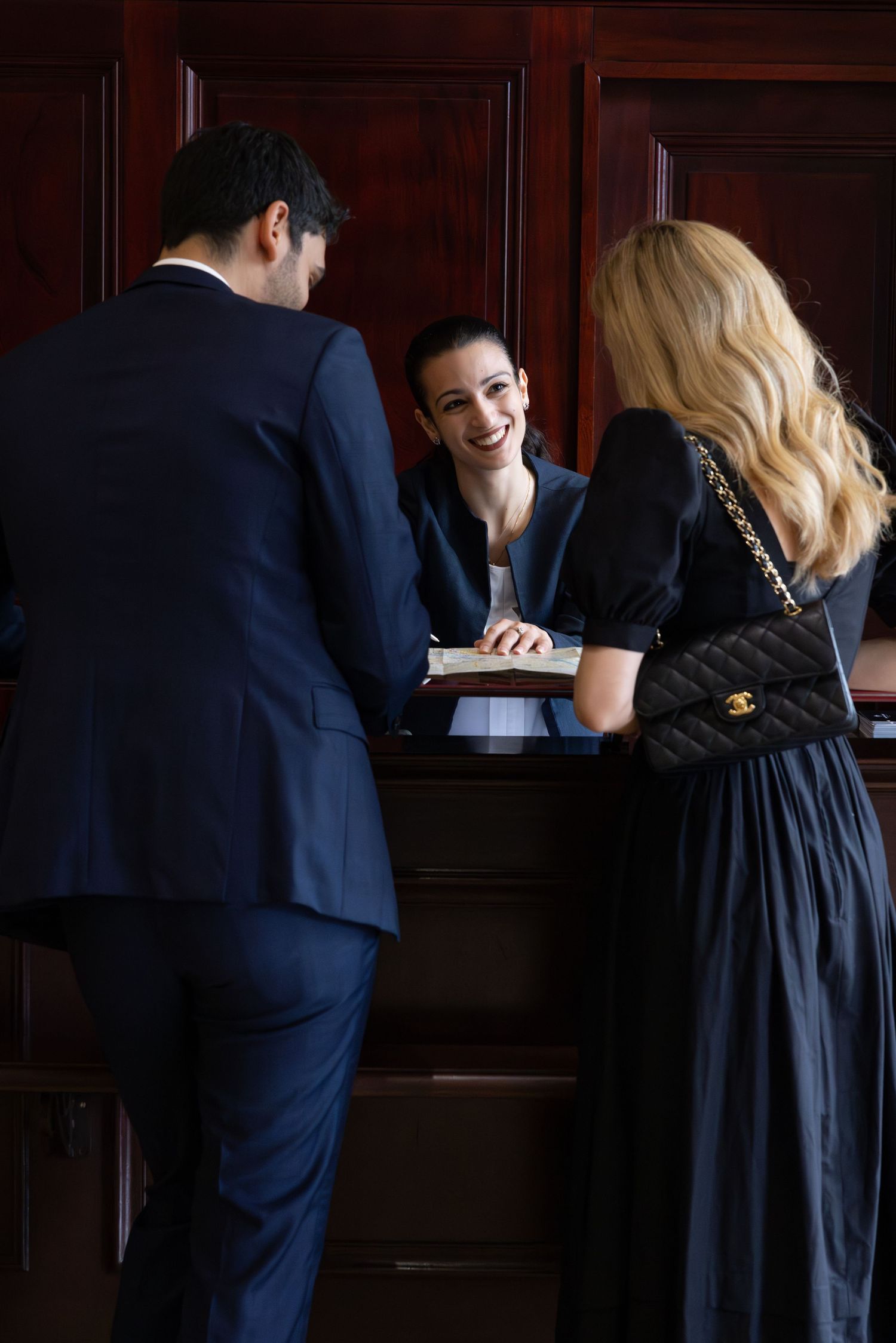 A couple checking in at a hotel reception desk with a smiling staff member behind the counter.