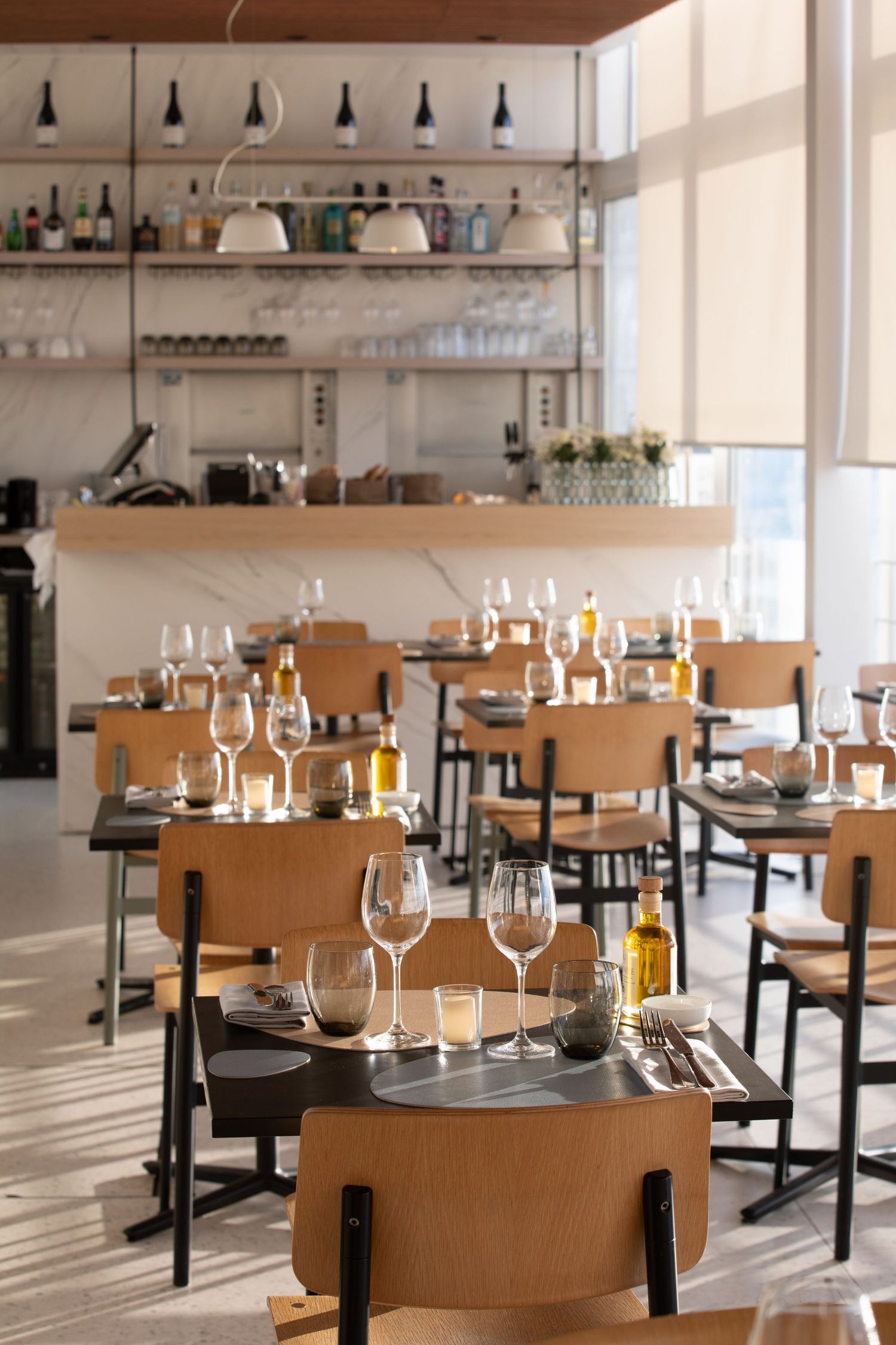 Modern restaurant interior with wooden tables, wine glasses, and pendant lighting creating an elegant dining atmosphere.