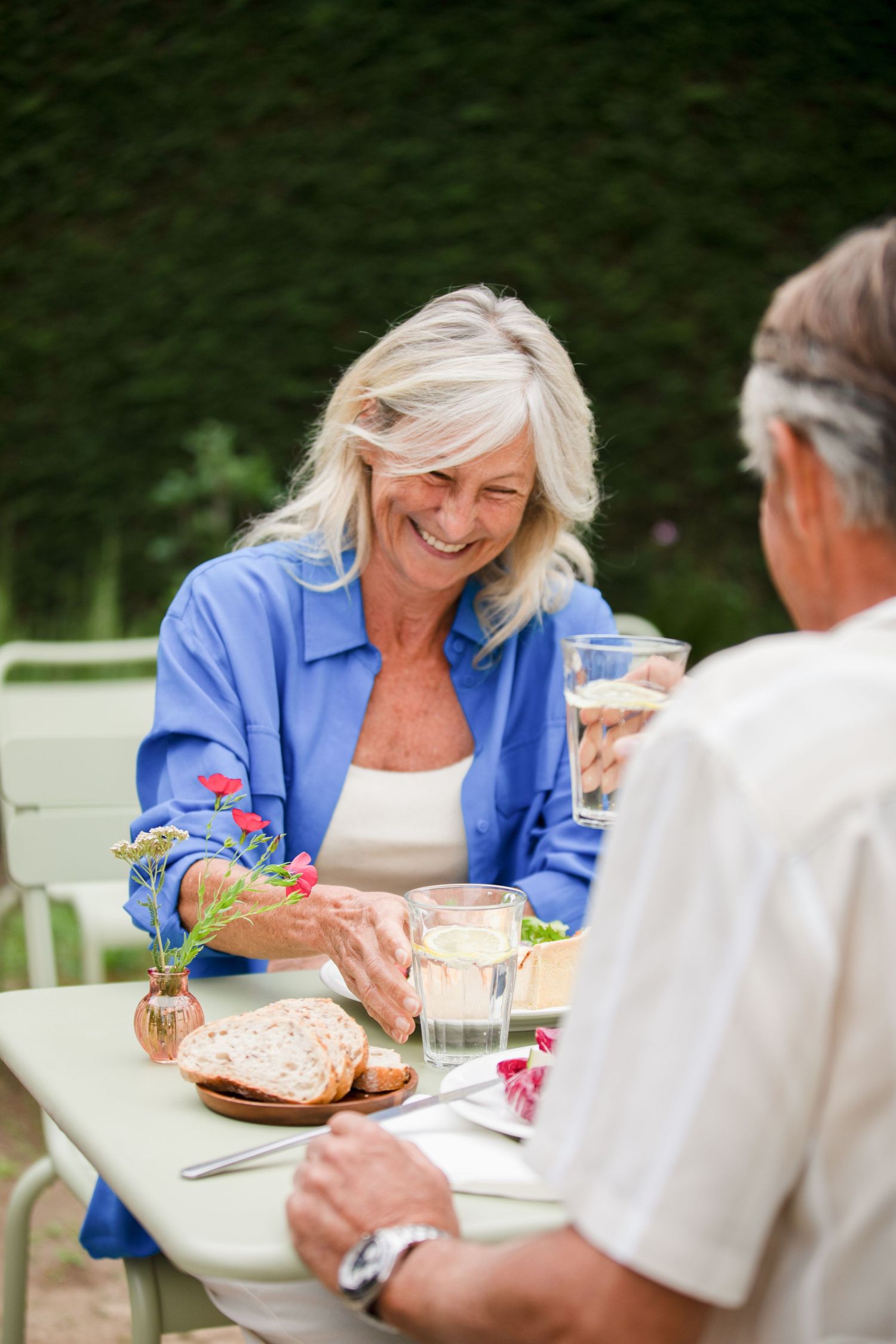A couple enjoys a casual outdoor meal together at a white table on a sunny afternoon.