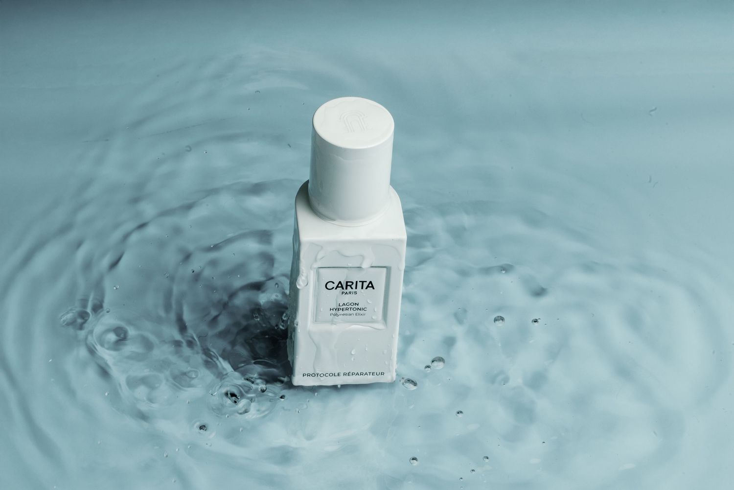 White cosmetic bottle labeled Capital floating on rippling turquoise water surface with splash effect.