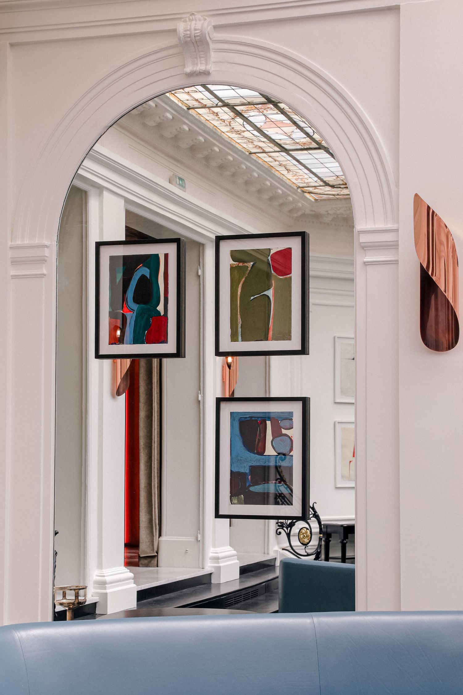 Interior hallway of a modern gallery space with white arched columns and framed artwork displayed on the walls.