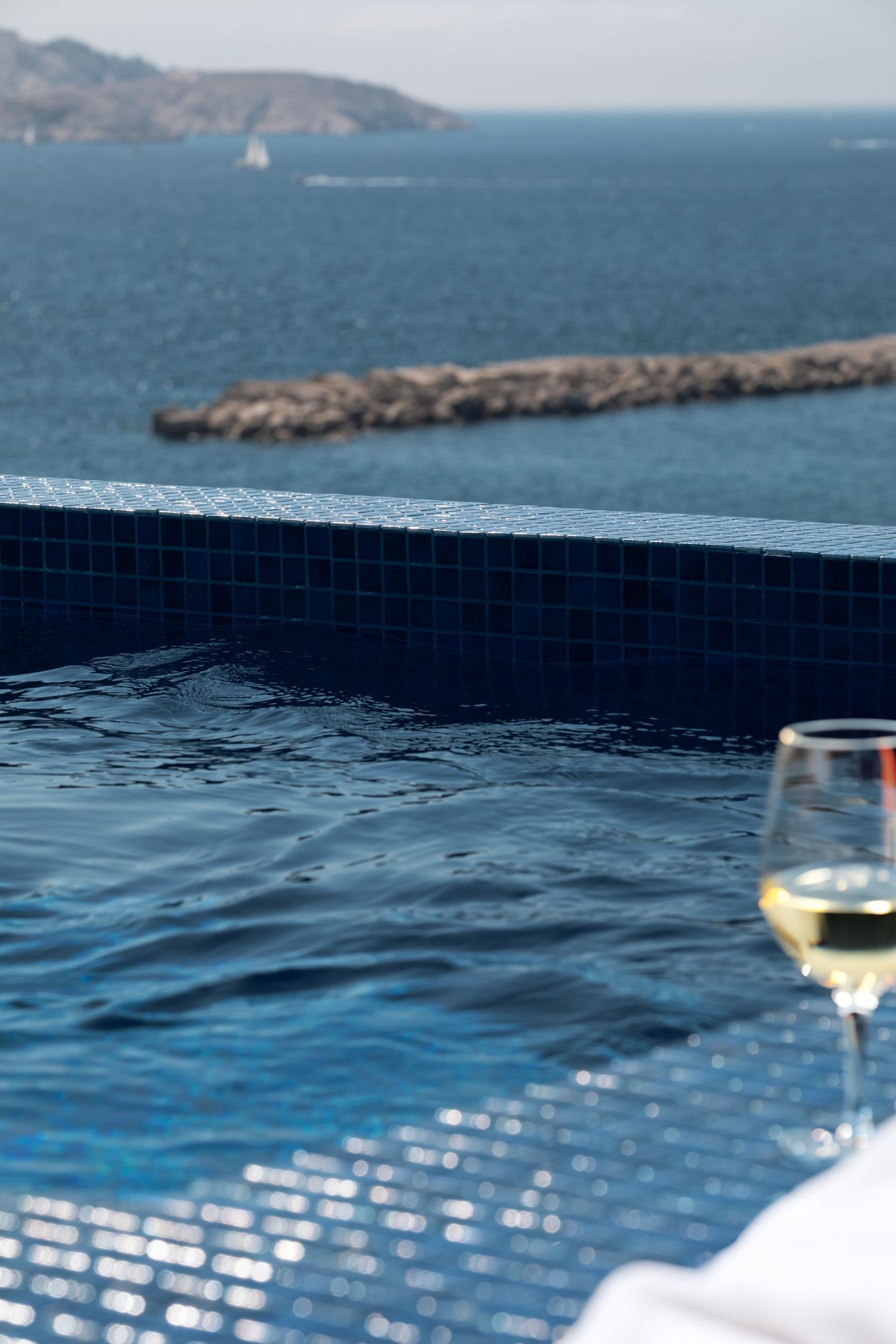 Infinity pool overlooking a scenic coastal landscape with mountains and blue ocean waters on a sunny day.