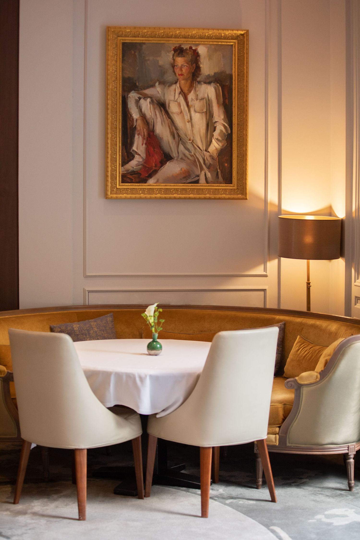 Elegant restaurant interior with white chairs around round table, vintage portrait in gold frame, and warm lighting.