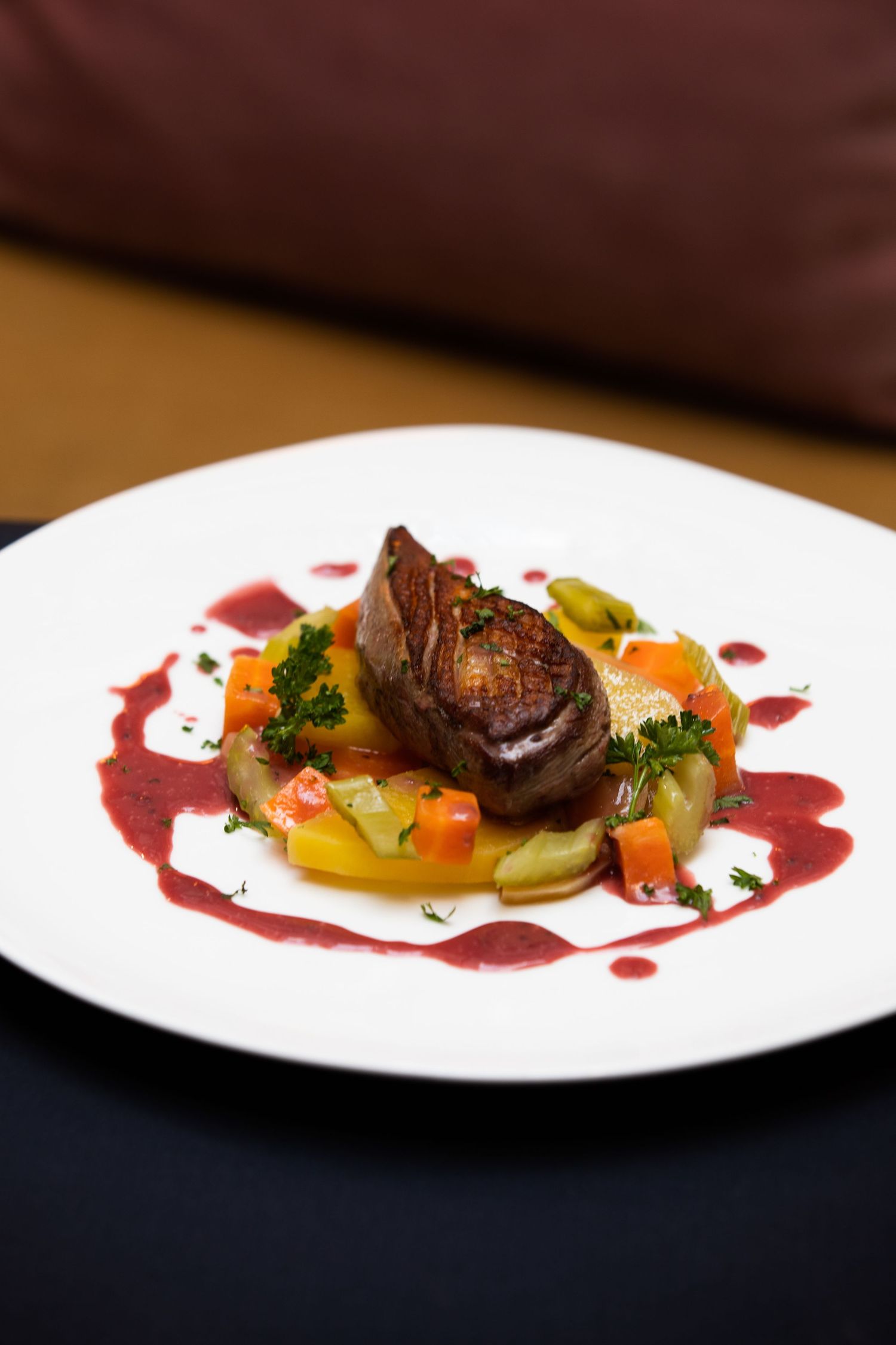 Elegant plated dish featuring seared meat with colorful vegetables and a vibrant red wine reduction sauce on white plates.