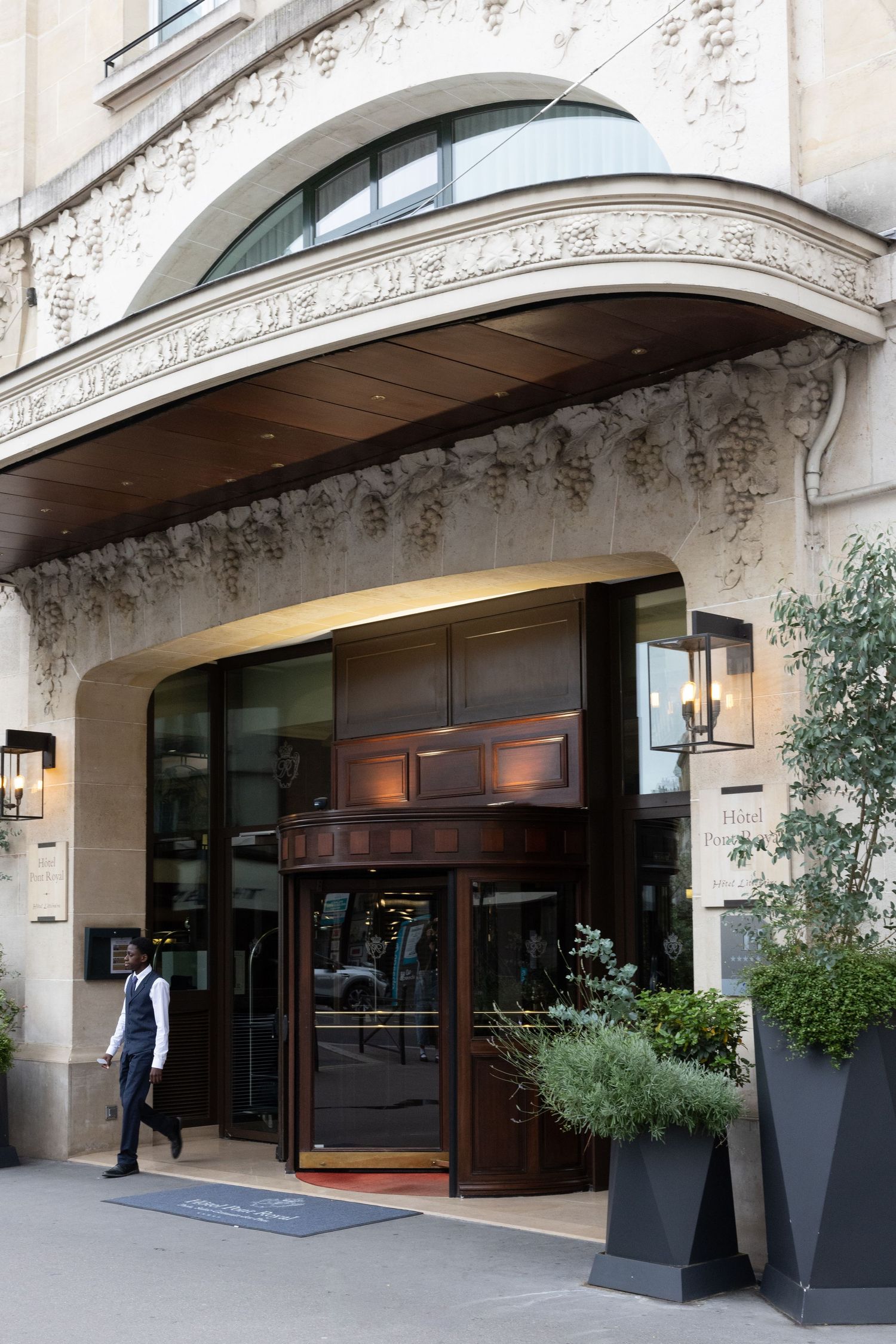 Elegant building entrance with ornate archway, revolving door, and decorative planters on a city street.