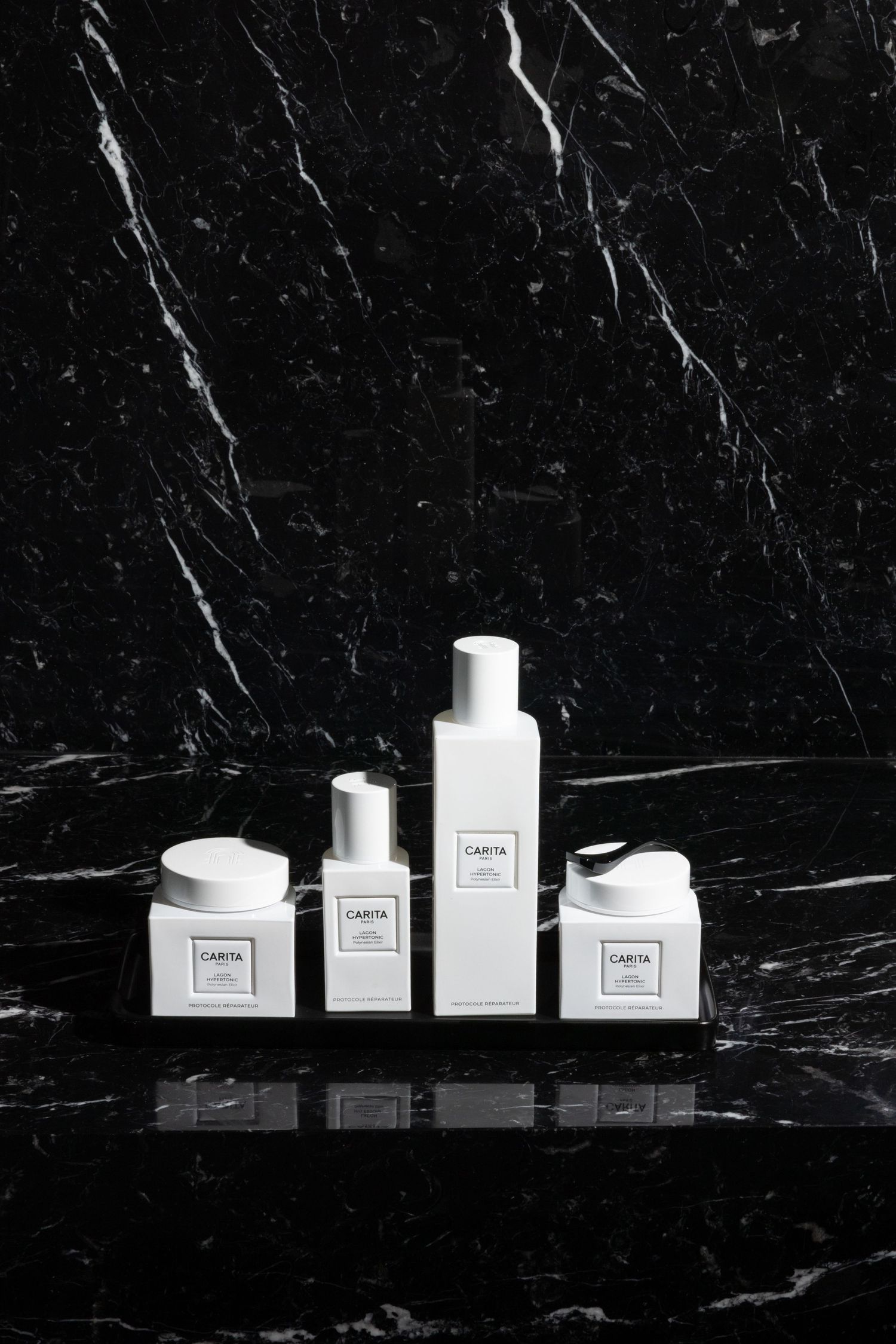 Minimalist white skincare product containers arranged on black marble surface in monochromatic aesthetic display.