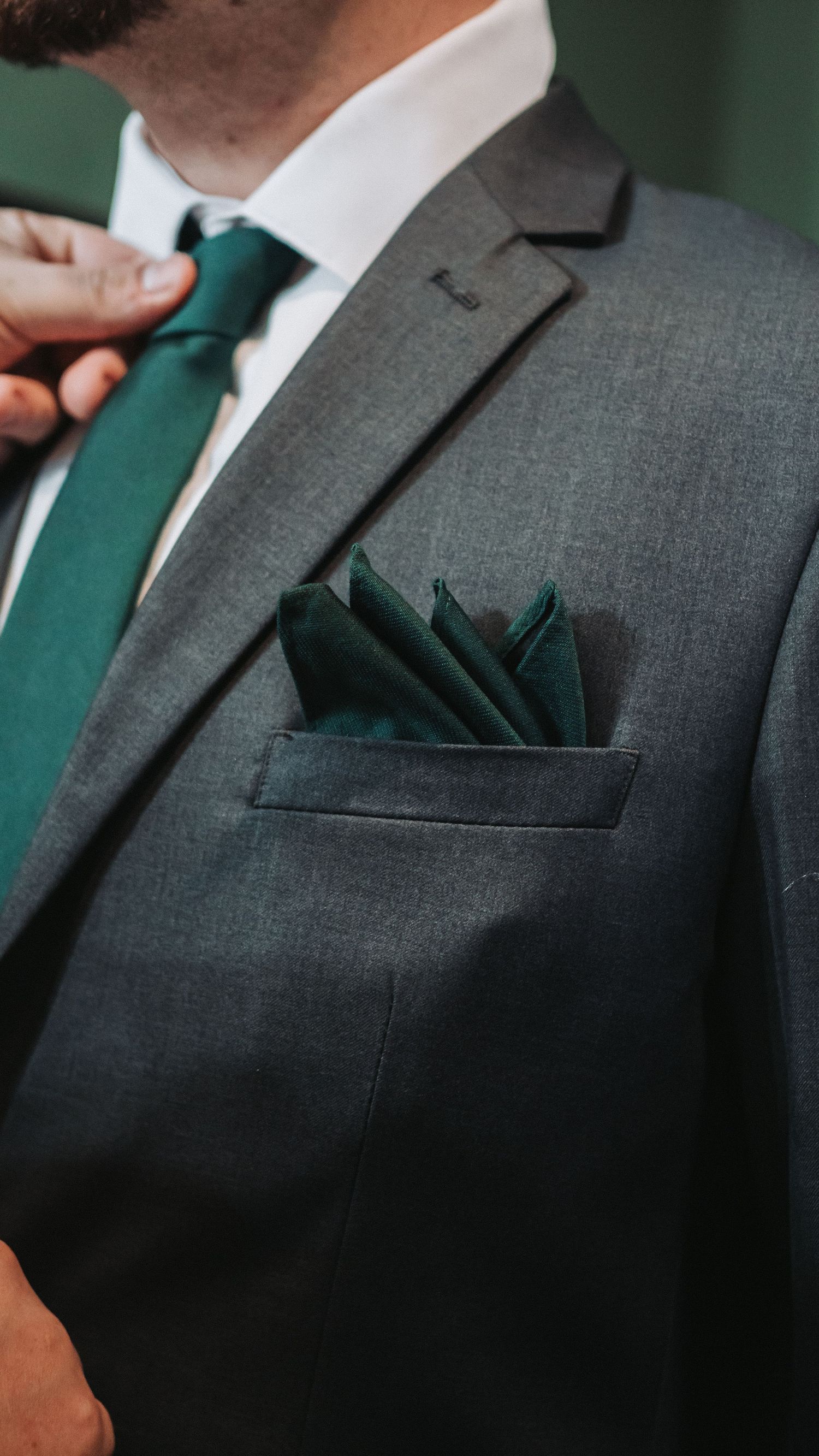 Man in gray suit with green silk pocket square and matching emerald tie, elegant formal attire detail.