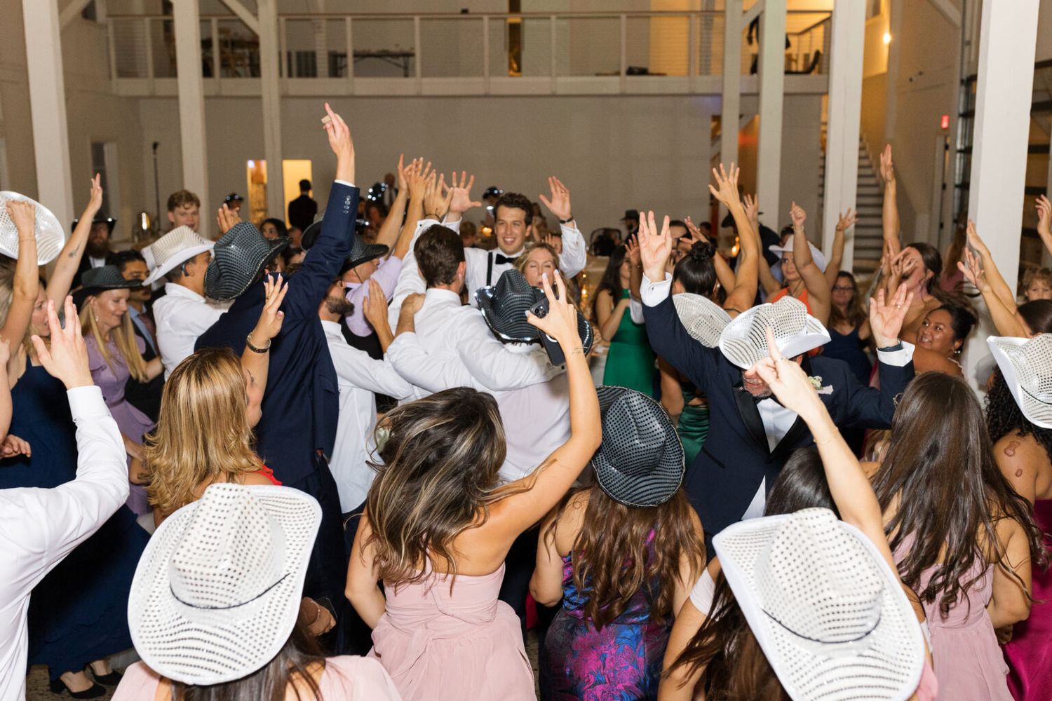 Guests dancing with hands raised at a lively wedding reception party indoors.