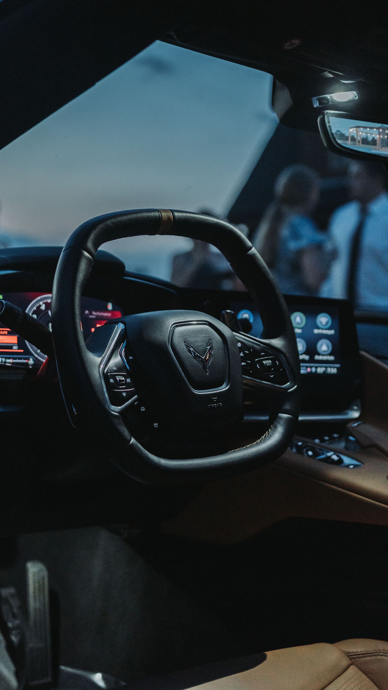Interior view of a Corvette C8 sports car featuring a black leather steering wheel, digital dashboard, and tan leather seats.