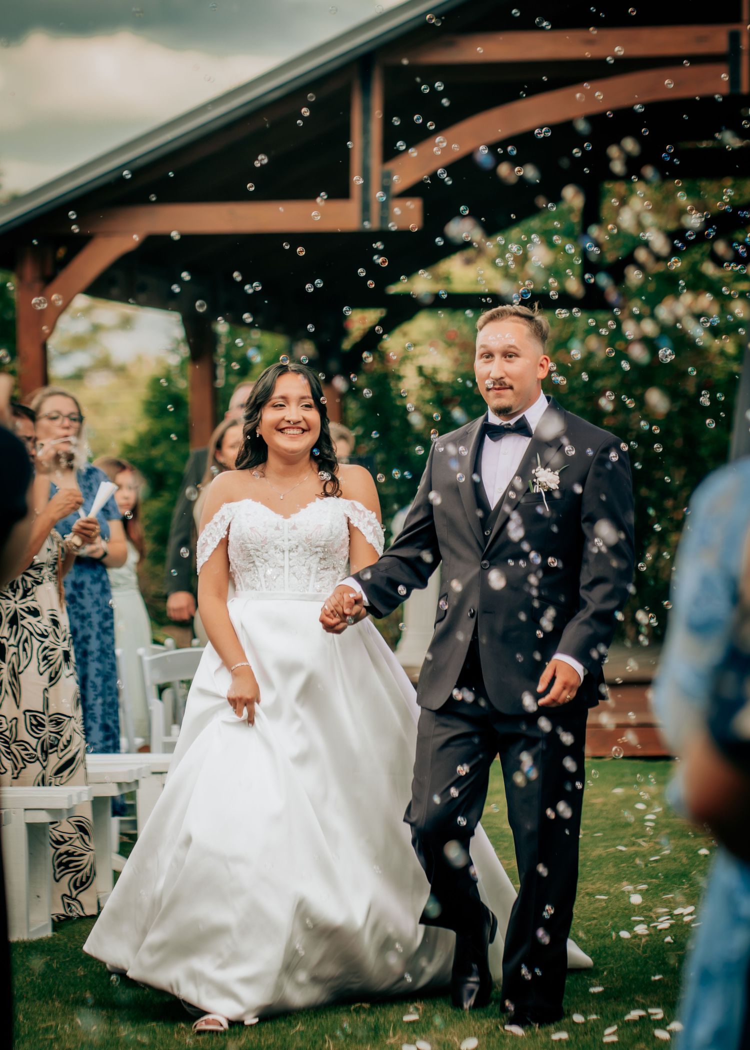 Bride and groom walk down the aisle surrounded by bubbles at an outdoor wedding ceremony.