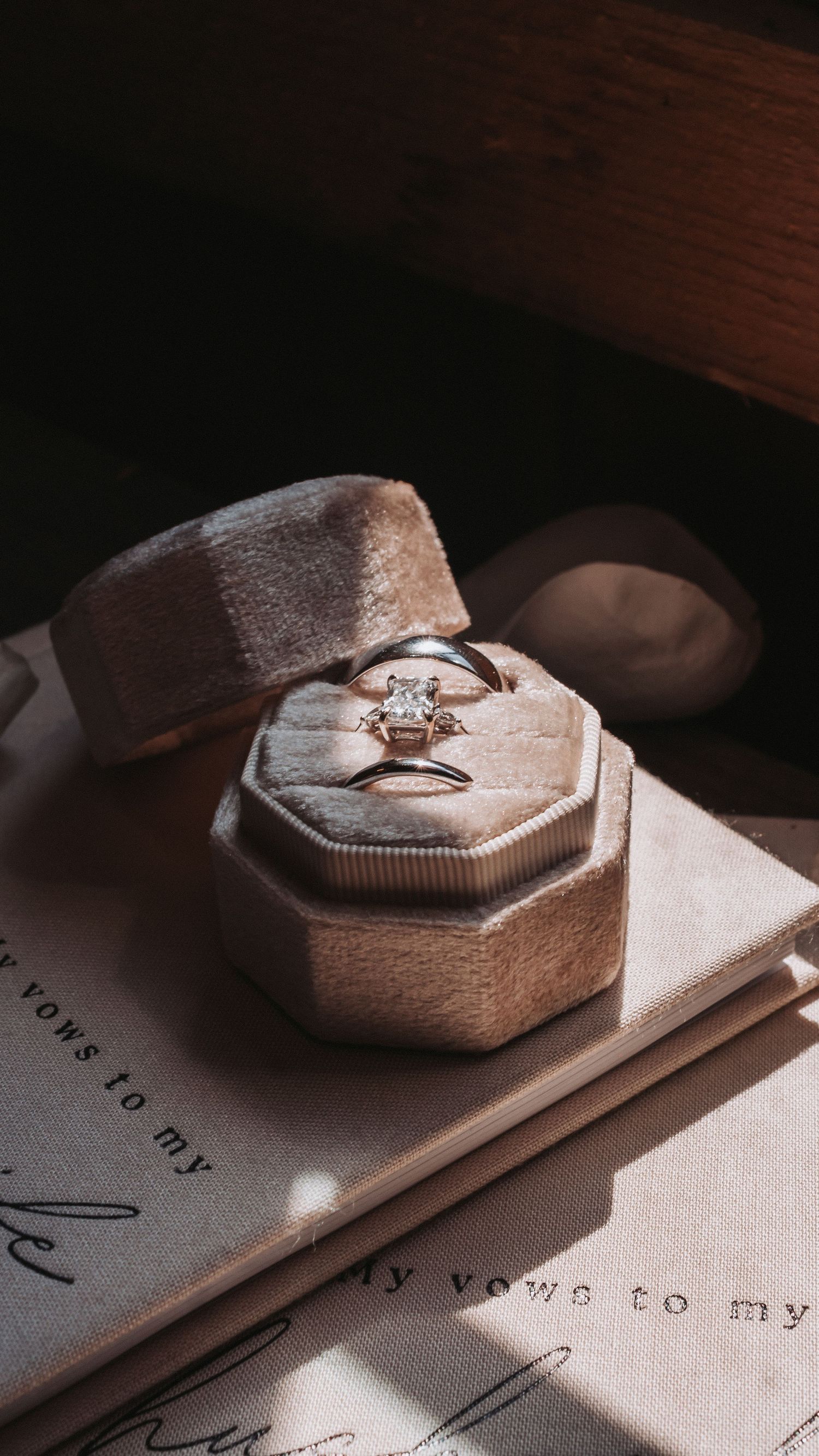 A diamond solitaire engagement ring displayed in a velvet octagonal ring box resting on a vow book.