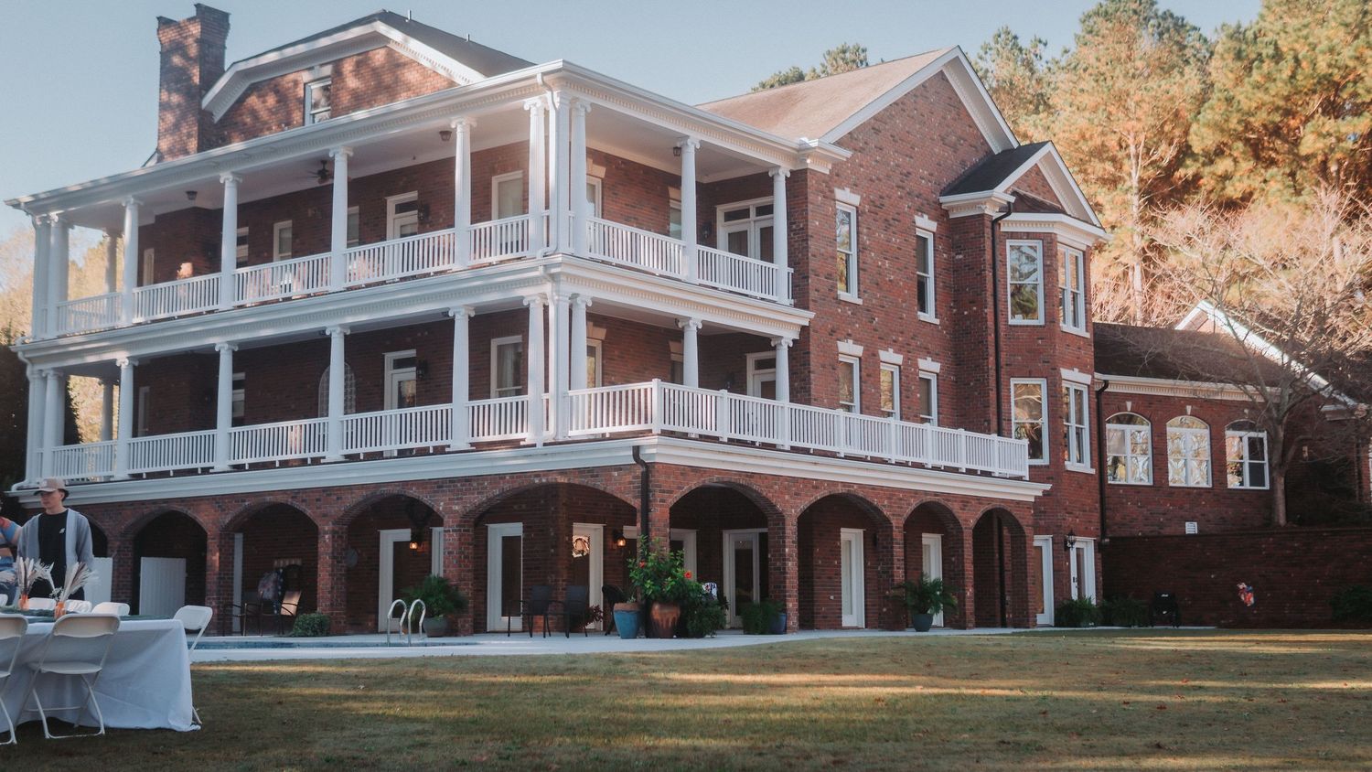 Elegant two-story brick mansion with white balconies and arched portico, surrounded by manicured lawn at dusk.