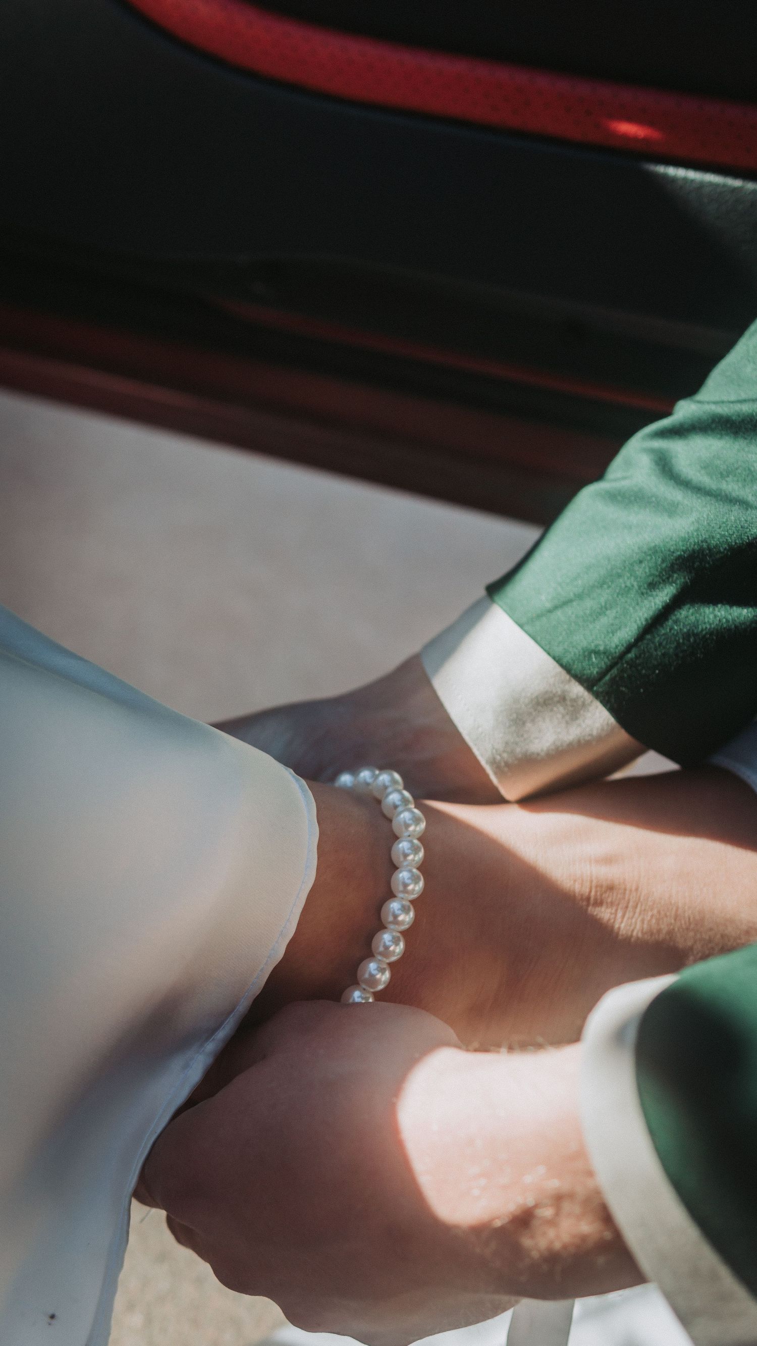 Two hands holding together, one wearing a delicate white pearl bracelet, with sunlight casting a warm glow.