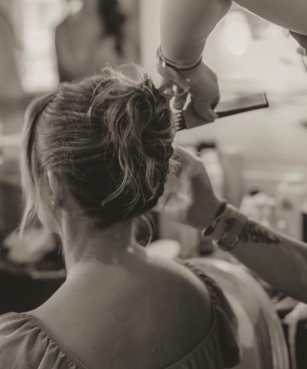 Black and white photo of a woman getting her hair styled in an elegant updo by a professional hairstylist.