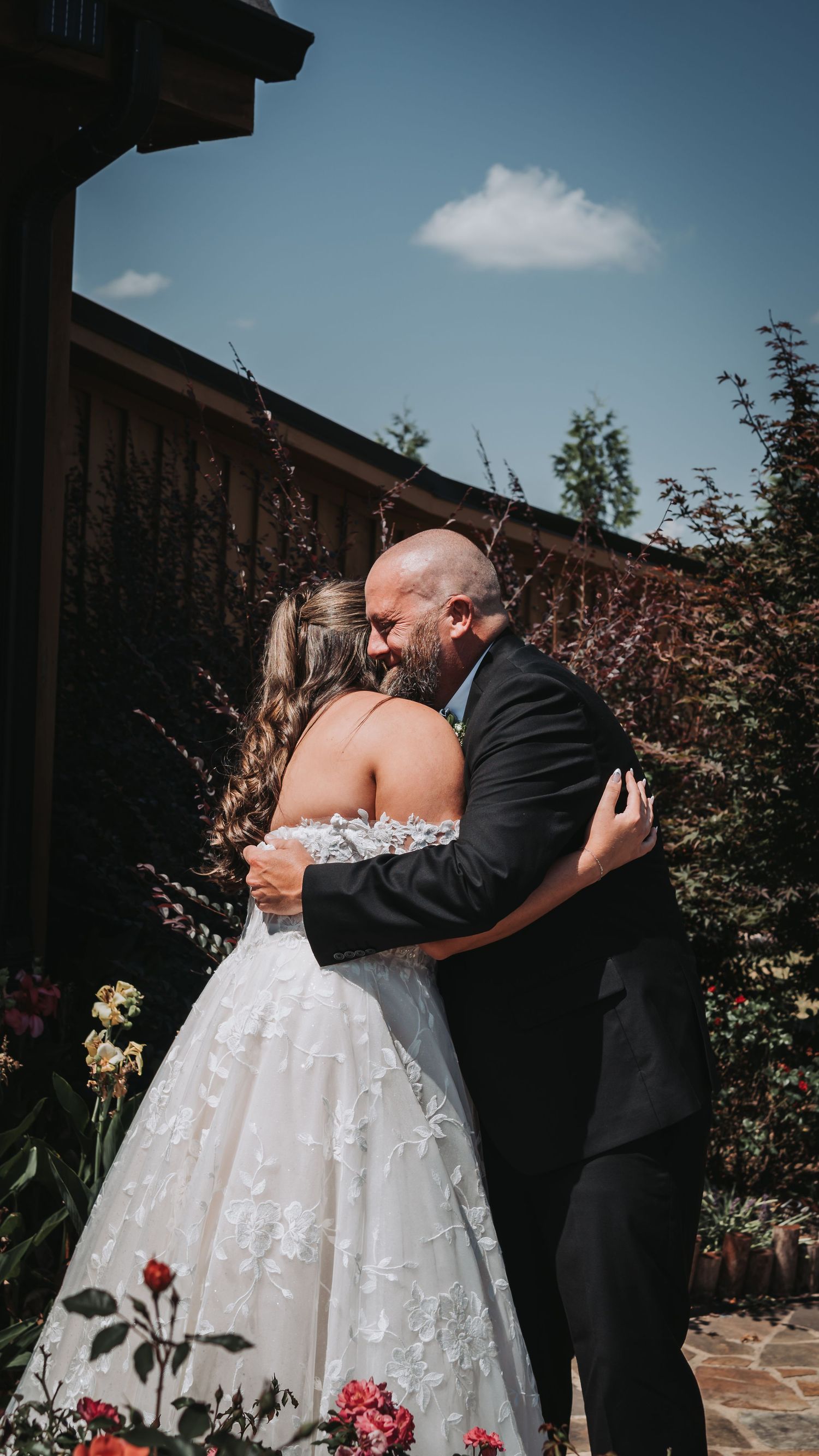 A bride and groom share an emotional first look embrace in a sunlit garden on their wedding day.