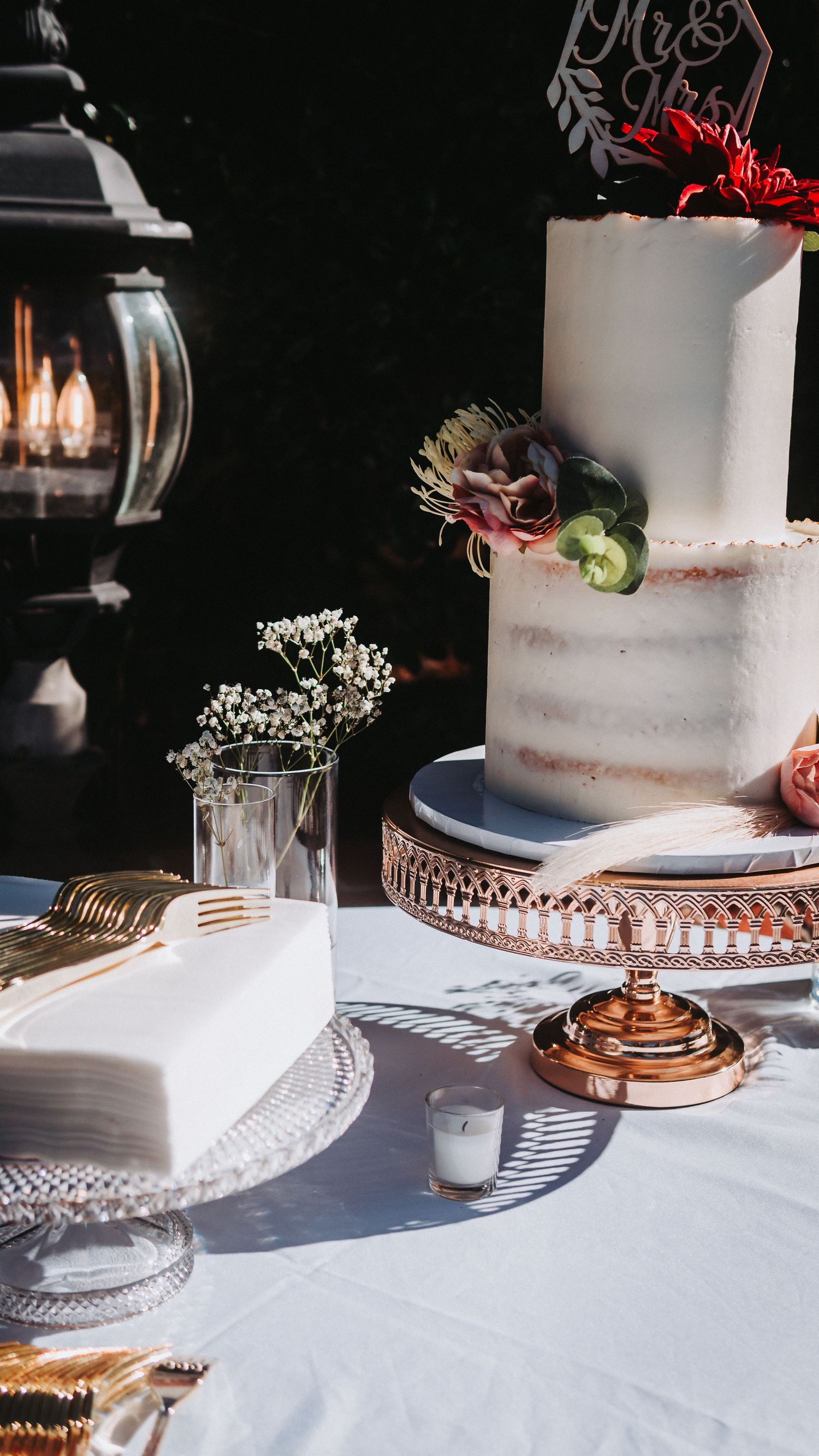 Elegant wedding cake table with a two-tier semi-naked cake topped with florals on a rose gold stand.