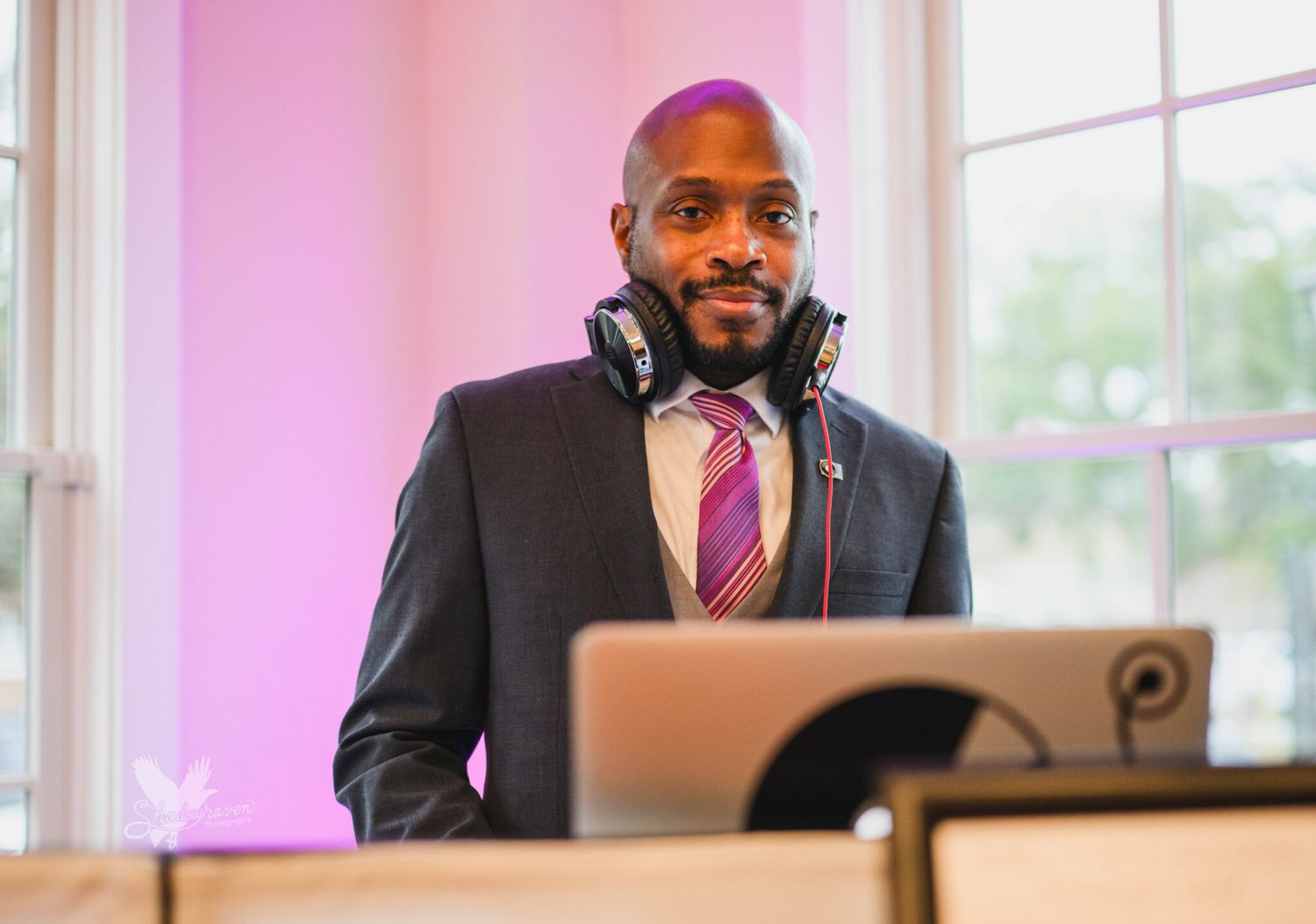 Professional DJ in a suit with headphones around his neck standing behind equipment at an elegant event venue.
