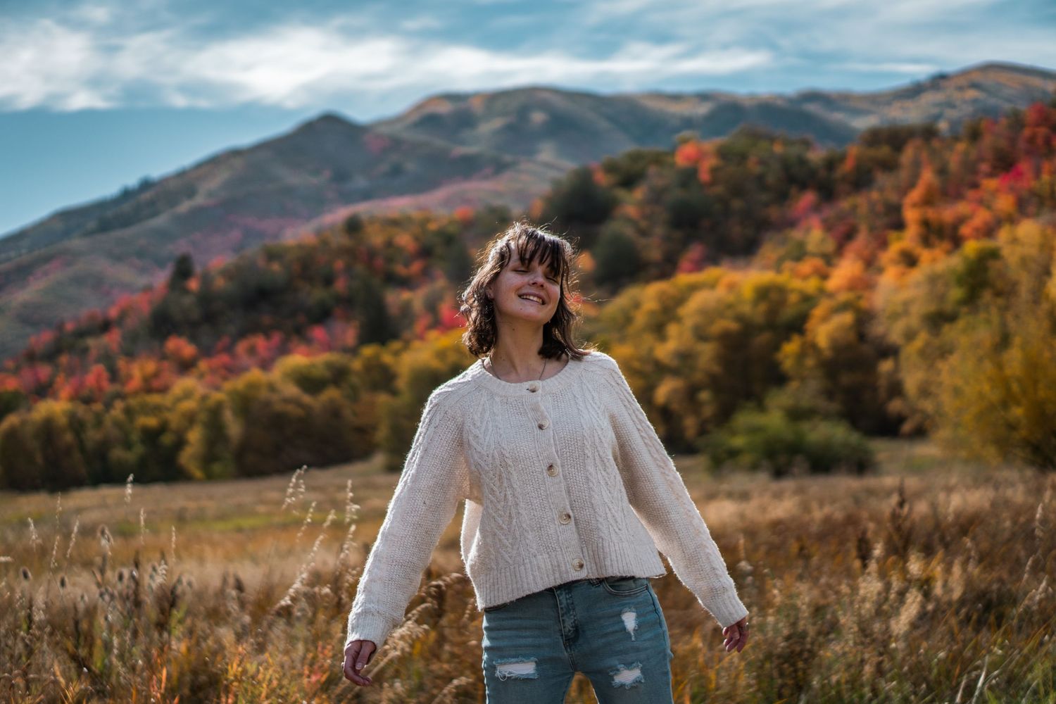 Kylee, a woman in her 20s smiling in the mountains surrounded by fall colors