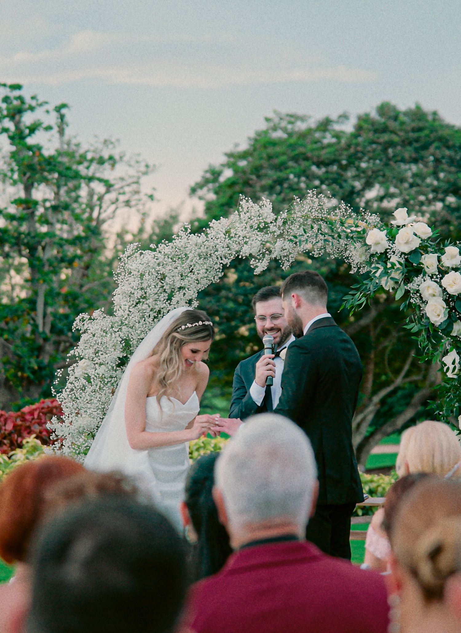 Wedding ceremony taking place under a beautiful floral arch with white baby's breath flowers in an outdoor garden setting.