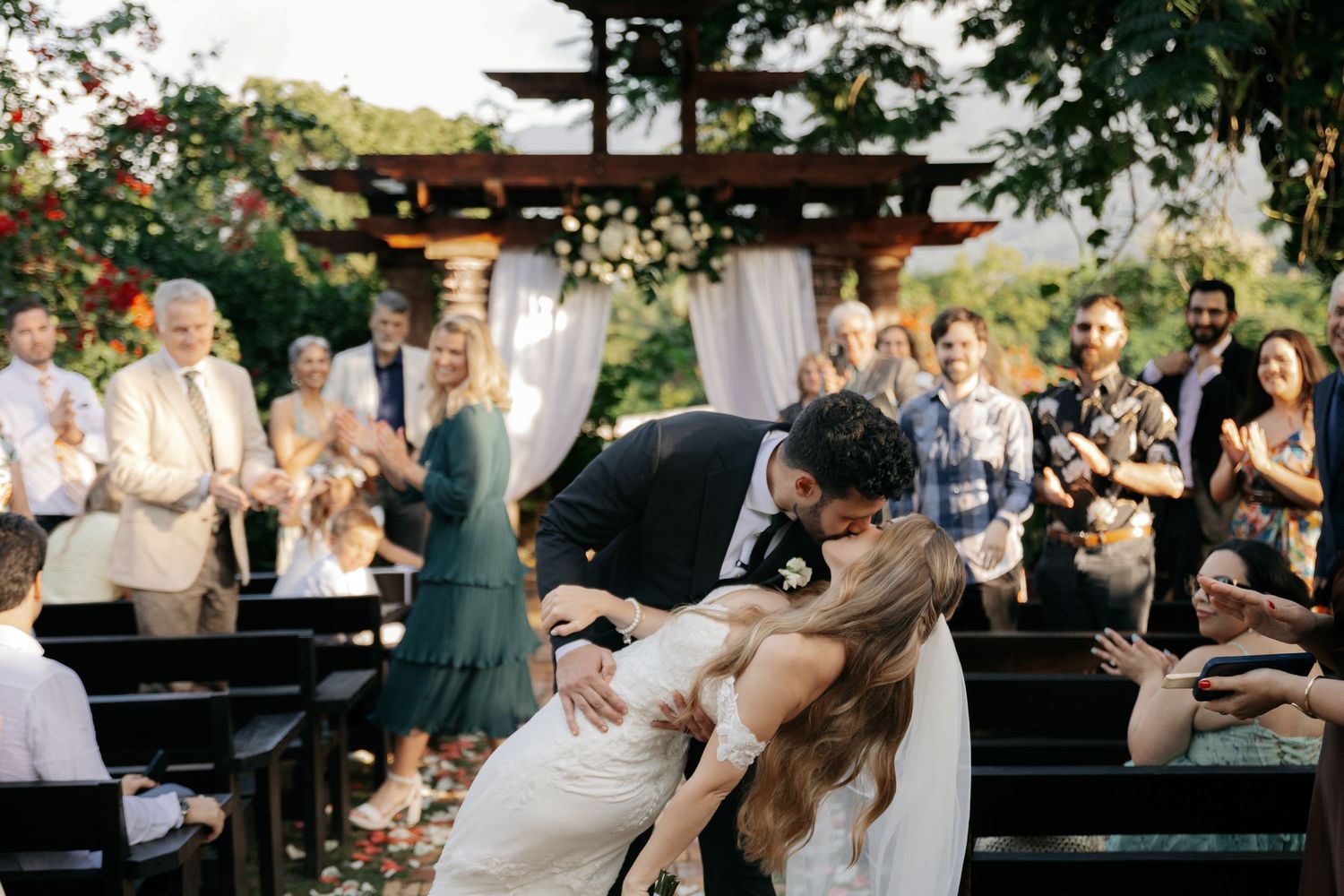 Outdoor wedding reception with guests dancing on a wooden deck surrounded by trees | POST-TALES WEDDS destination wedding photography.