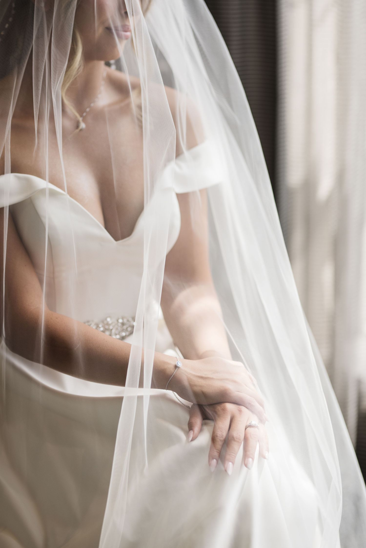 Close-up of bride in strapless sweetheart gown draped in flowing white veil with delicate satin edge detail.