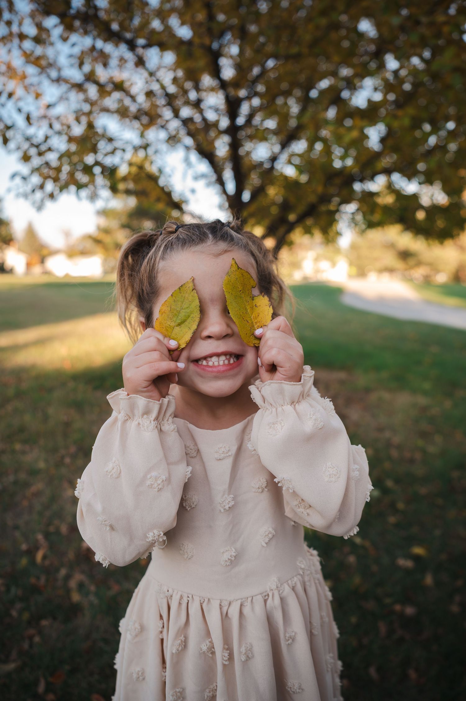 A playful moment outdoors holding autumn leaves up to their eyes while wearing a white vintage-style dress.