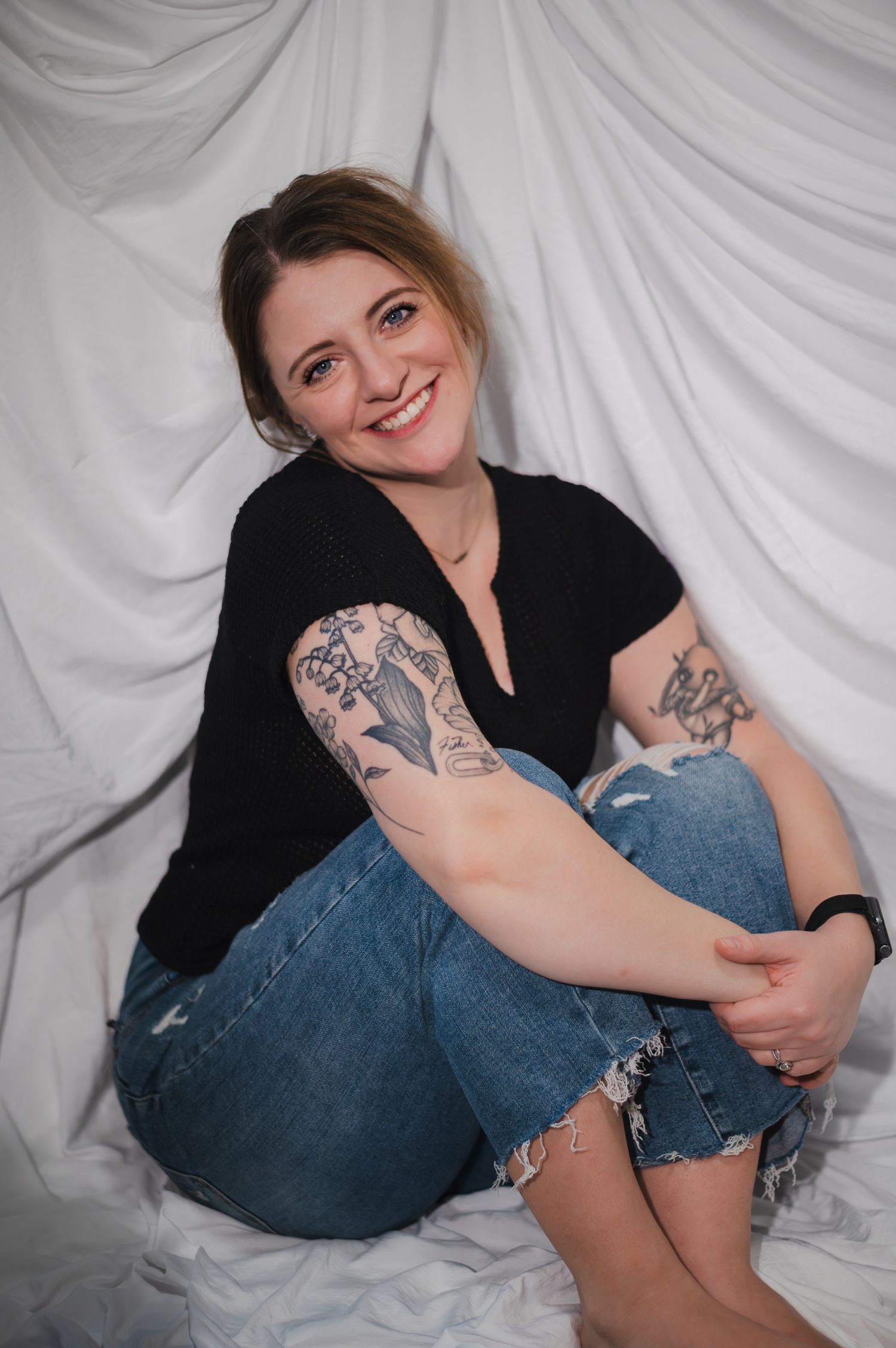 Studio portrait of a photographer with white backdrop showing relaxed seated pose.