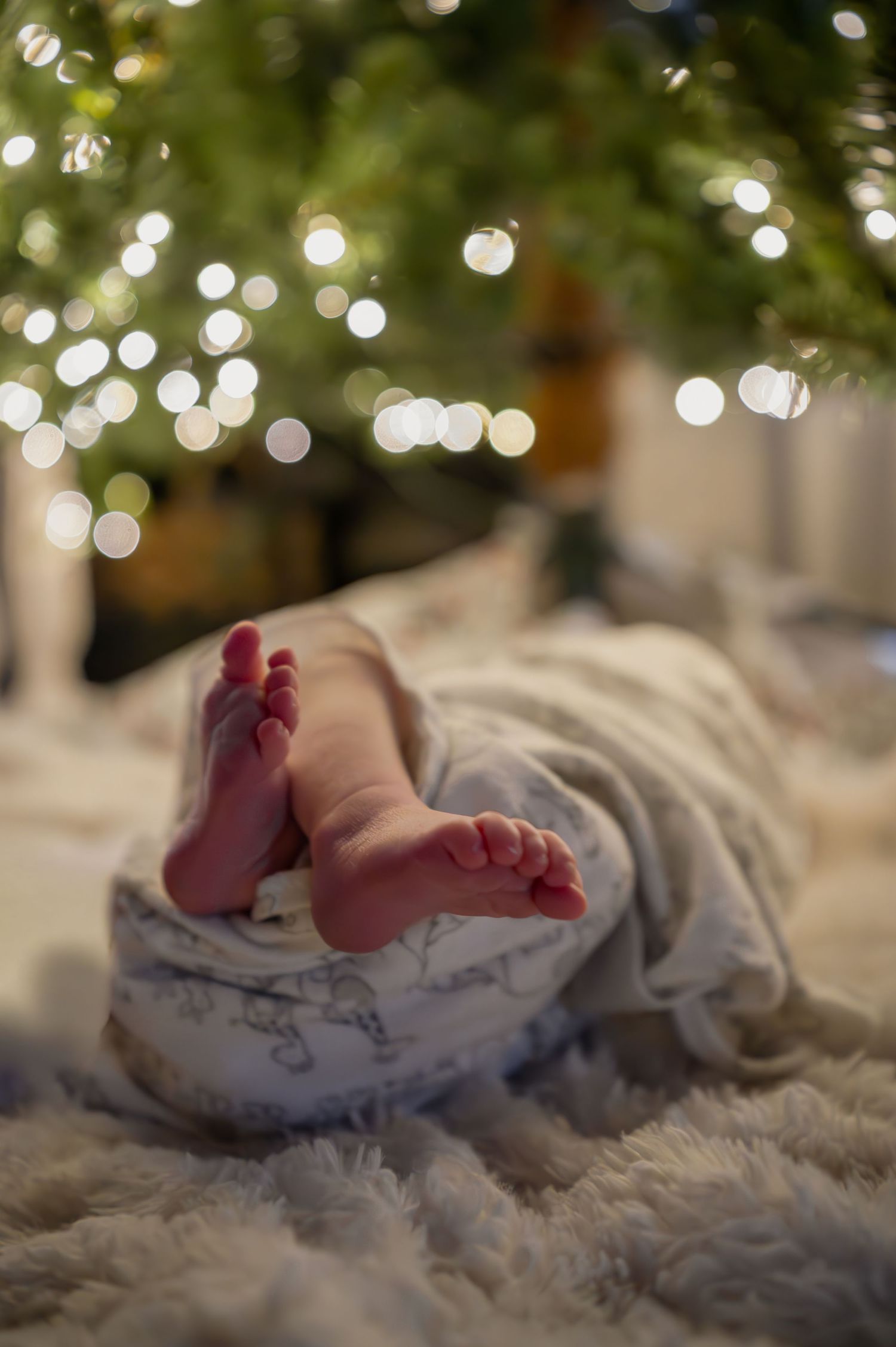 Baby feet peeking out from blanket with soft bokeh lights in background.