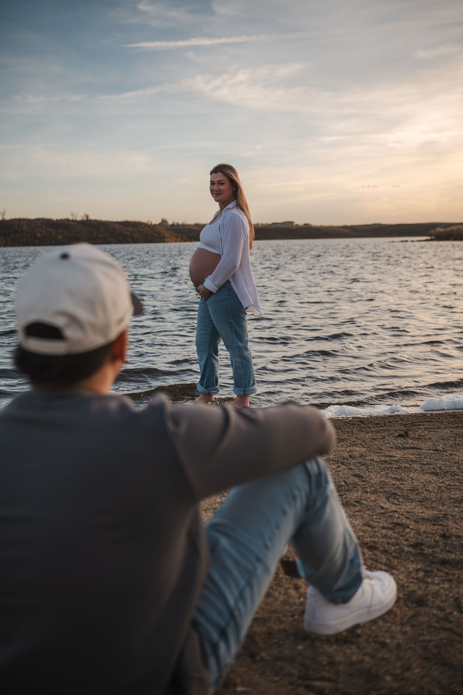 People relaxing on shoreline at sunset with lake and hills in background.