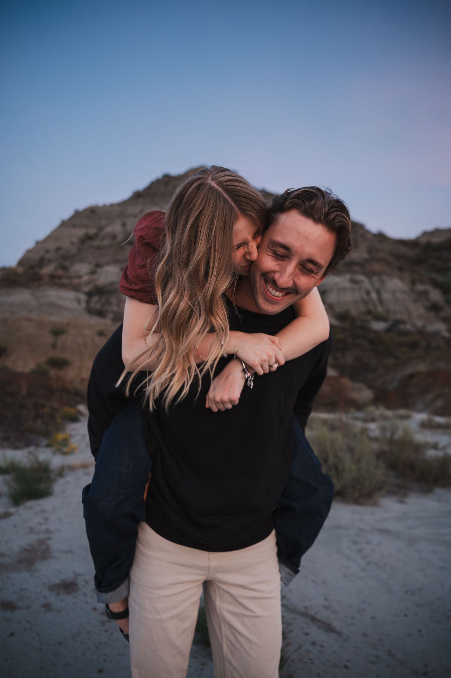 Couple sharing playful piggyback moment against desert mountain backdrop at sunset.