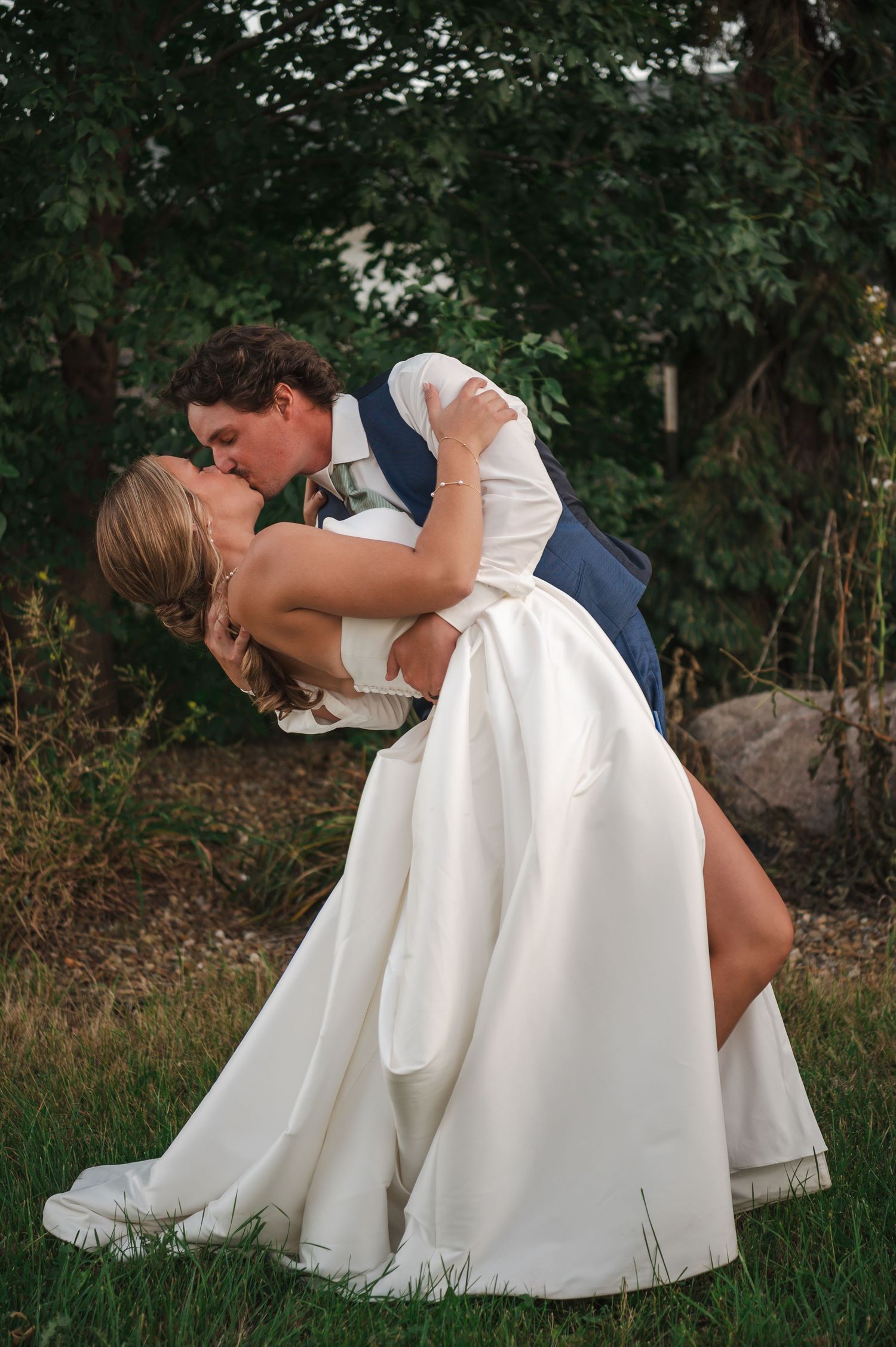 Romantic dip kiss between newlyweds in garden setting.