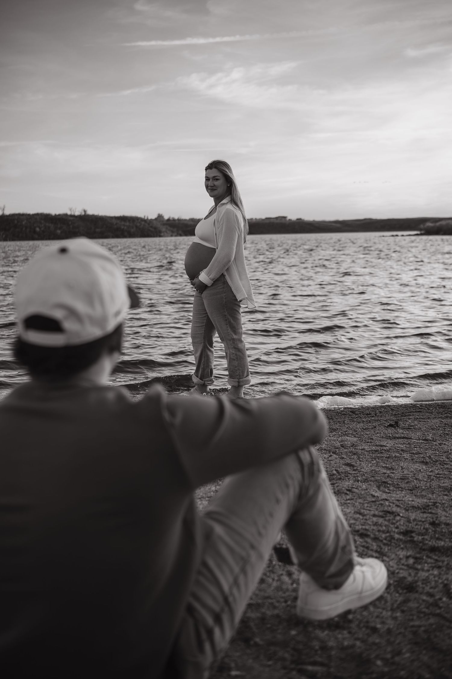 Black and white photo of people sitting by a serene lake at sunset.