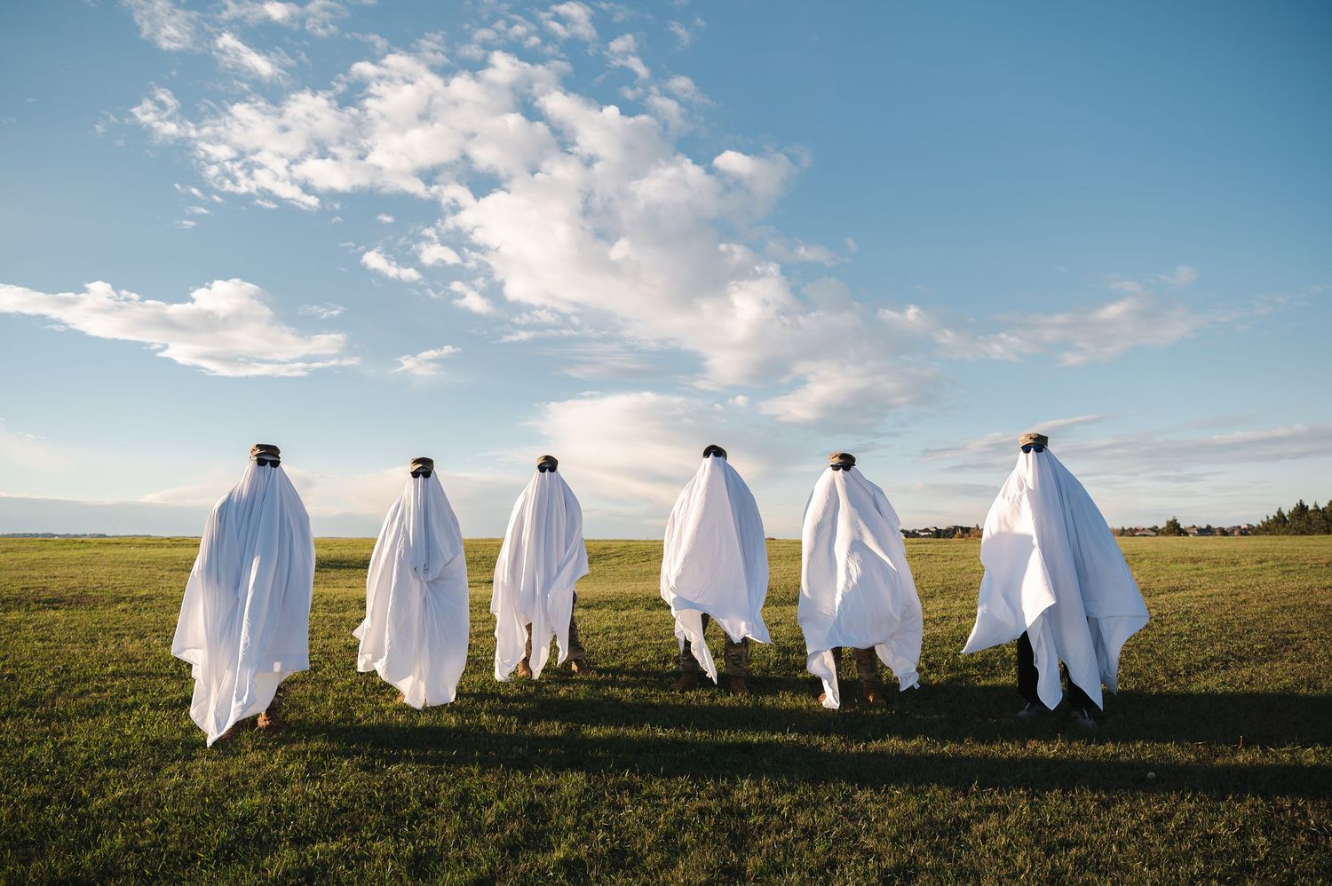 Row of people wearing white ghost costumes in a sunny field.