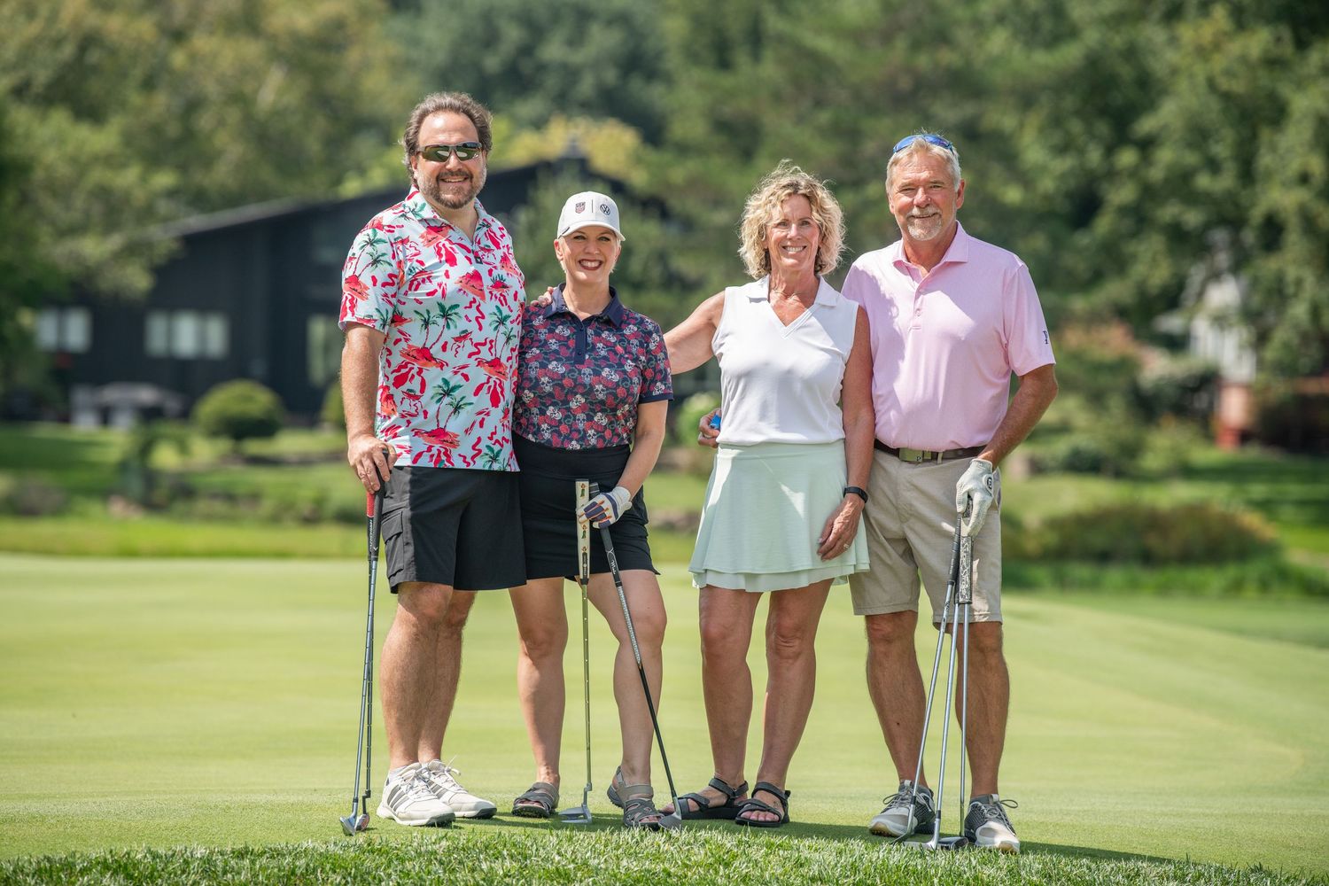Four golfers smiling together on lush green golf course on a sunny summer day.
