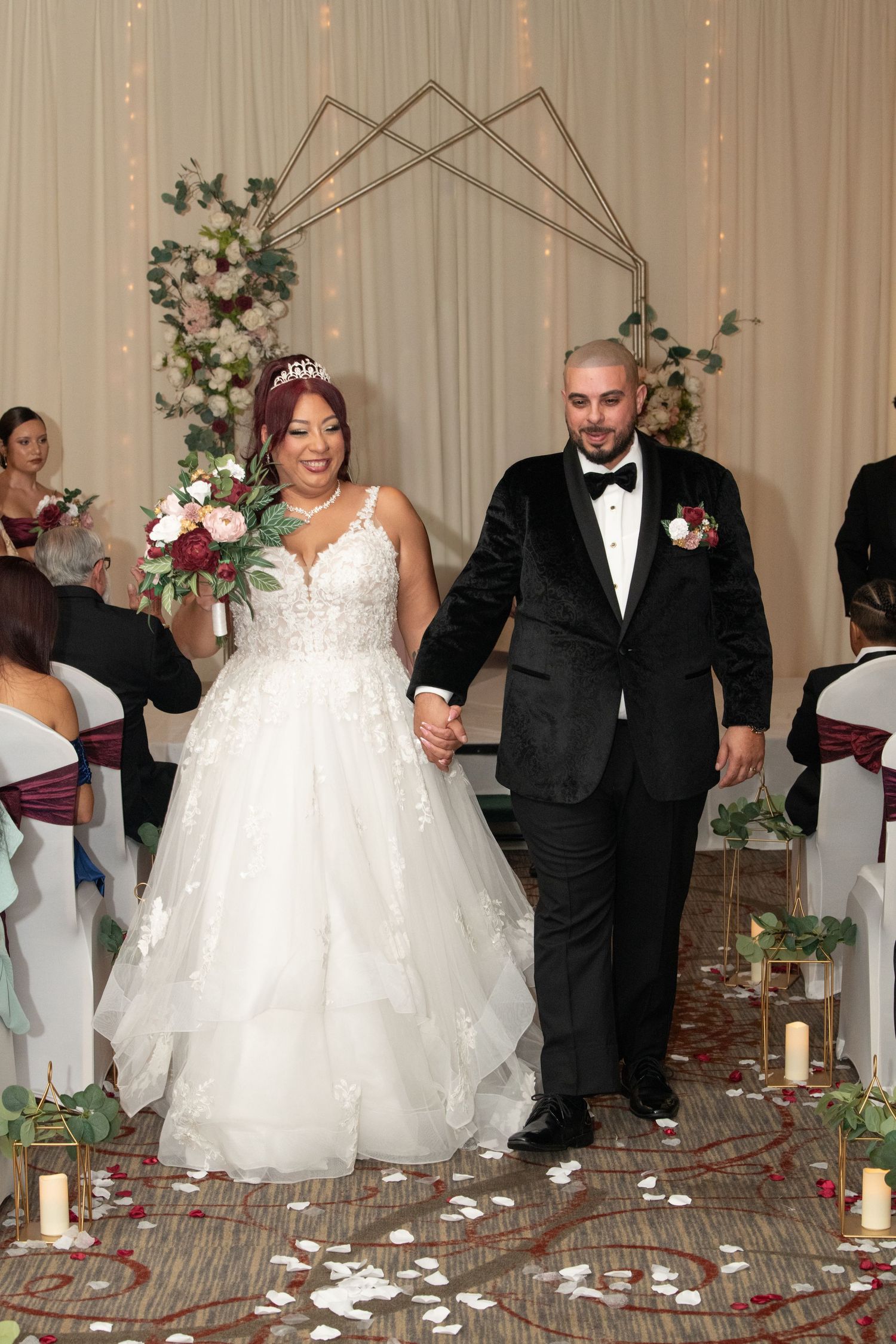 Bride and groom walk down the aisle hand in hand at an elegant indoor wedding ceremony with floral arch.