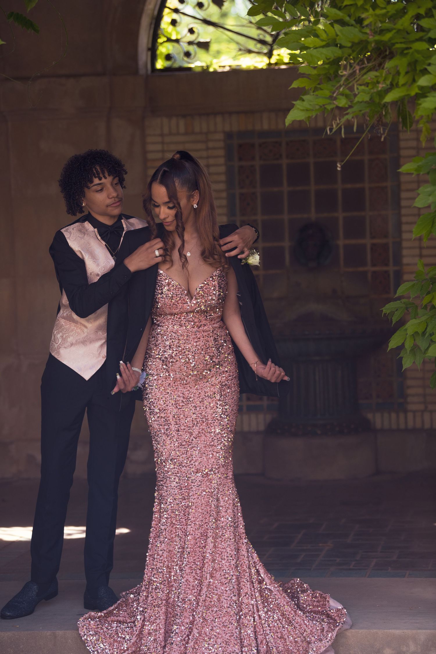 Prom couple posing together, young man in tuxedo placing corsage on woman in pink sequin gown.