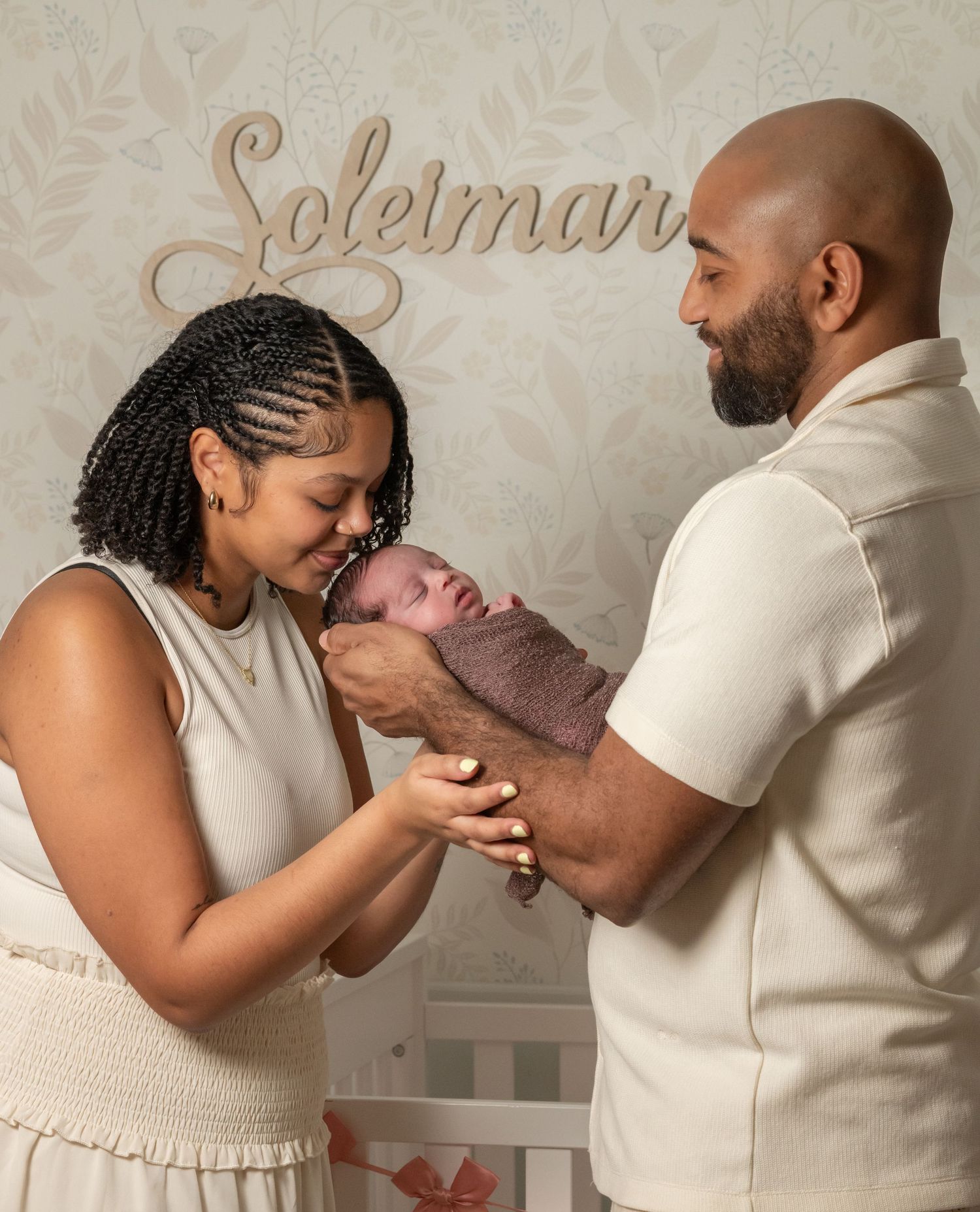 New parents tenderly admire their swaddled newborn baby in a nursery decorated with name sign.