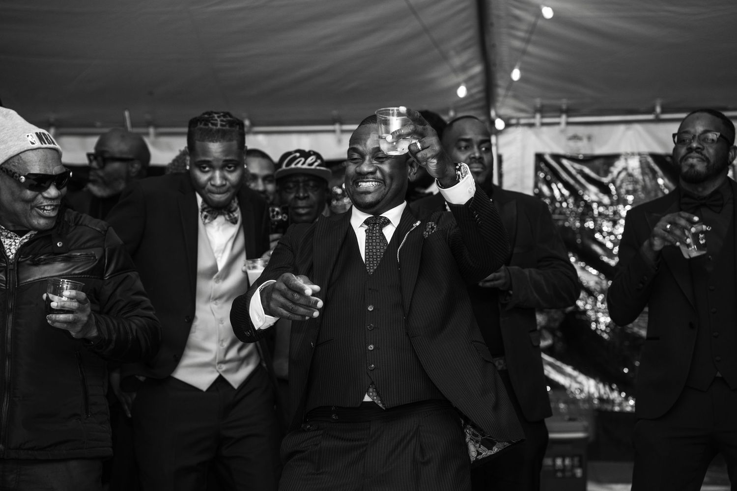 Black and white photo of men in suits celebrating at a formal event under a tent.