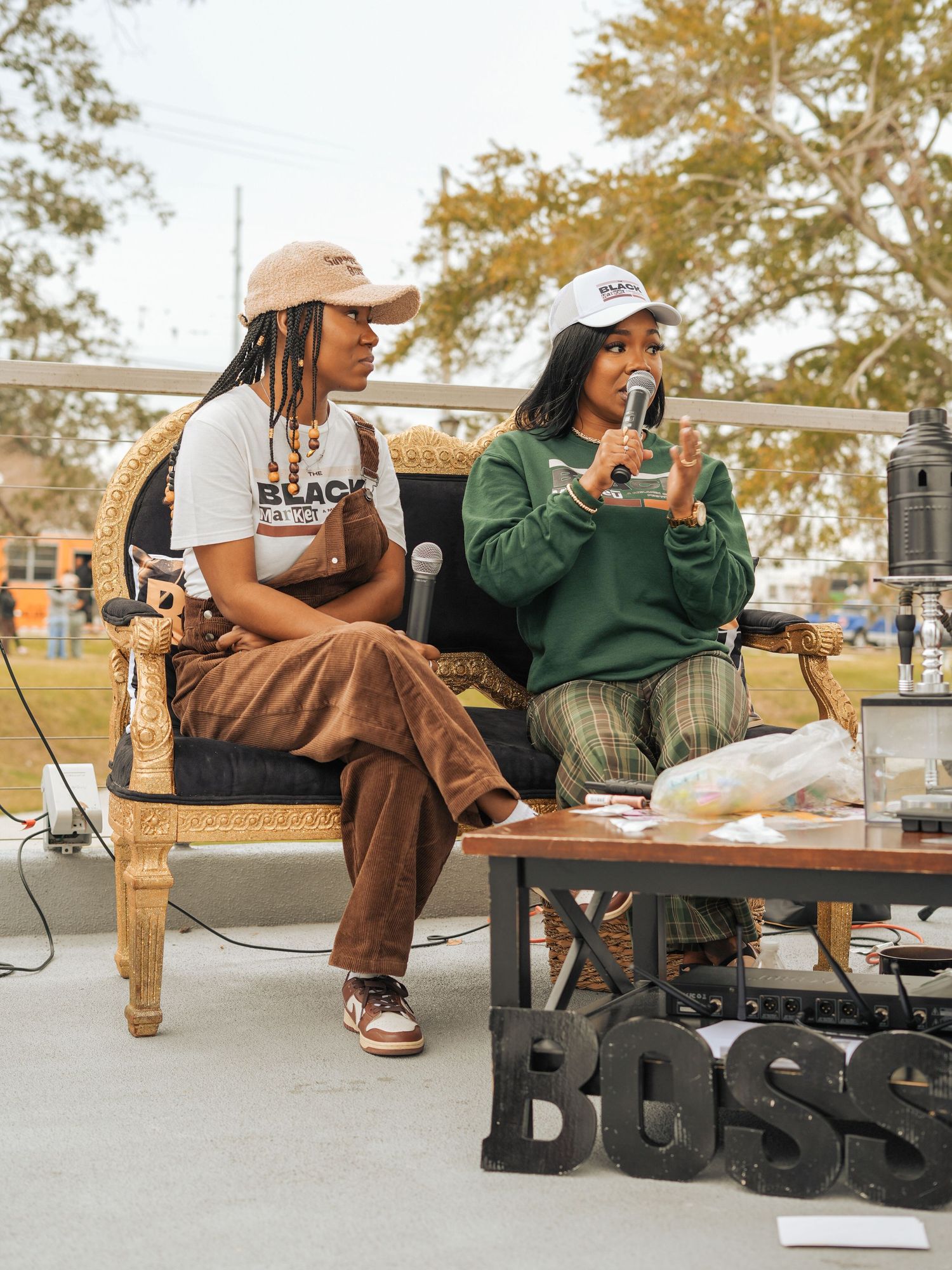 Two people relax on a wooden bench while enjoying beverages and snacks outdoors.