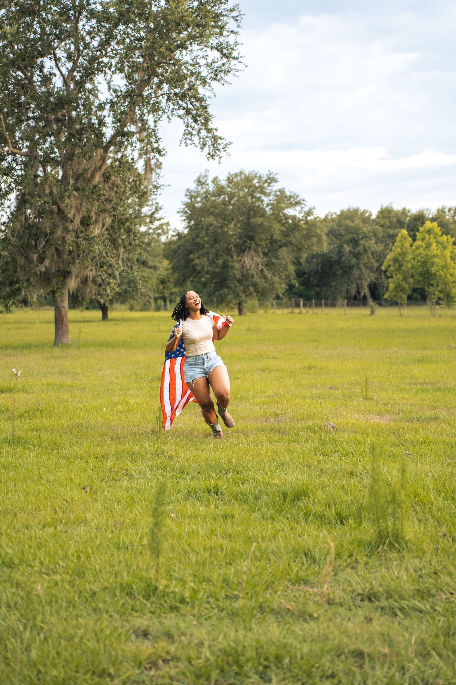Woman running through green field holding American flag on sunny day with trees in background at Farmettes Photo Studio
