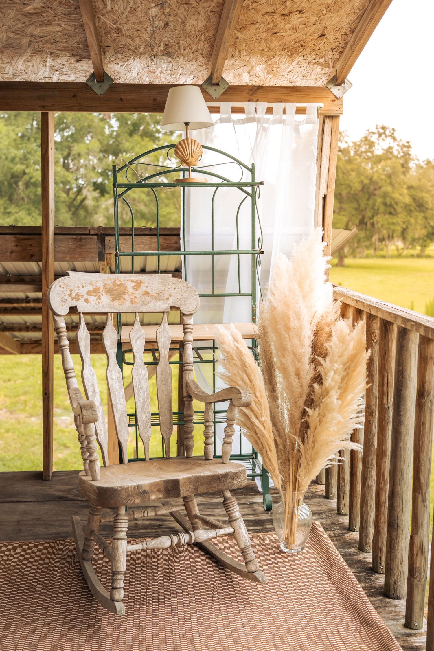 Rustic wooden rocking chair on a farmhouse porch with pampas grass decor and vintage iron bed frame backdrop at Farmettes Photo Studio