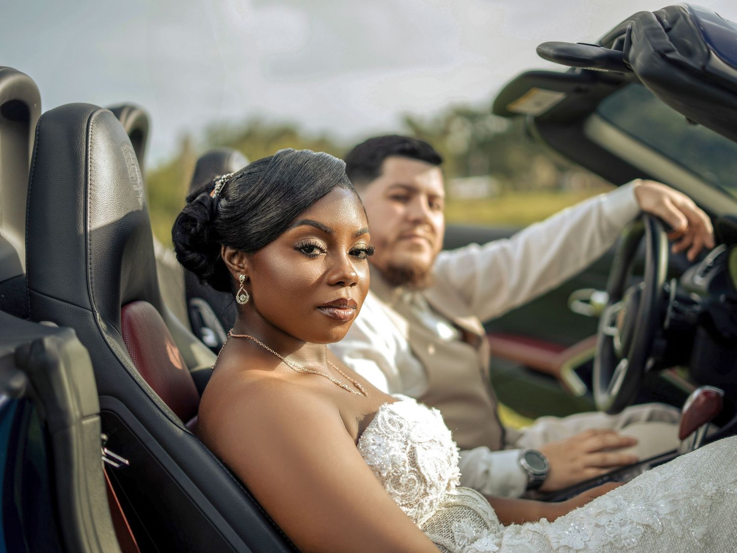 Bride and groom posing in a luxury convertible sports car on their wedding day.