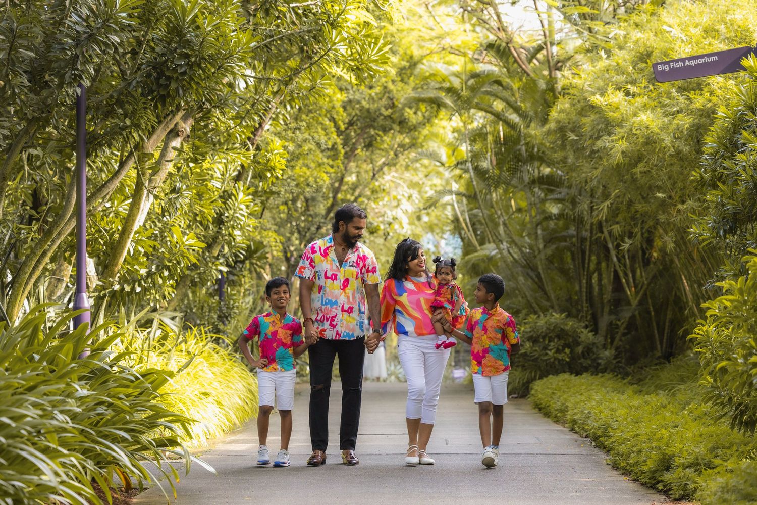 People walking together on a lush green path surrounded by trees on a sunny summer day.