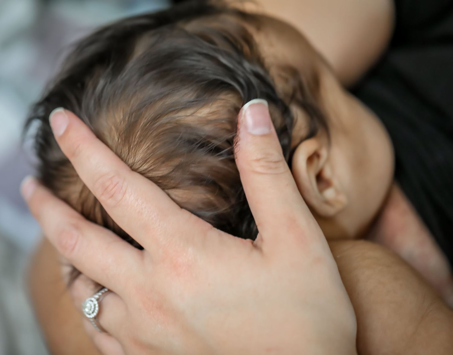Close up of a hand with an engagement ring gently caressing a sleeping baby's head.