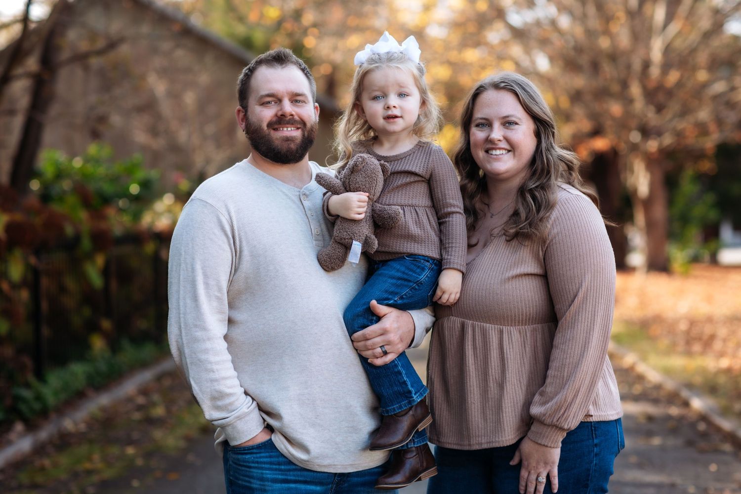 A family stands together outdoors on an autumn day wearing coordinating neutral-colored sweaters.