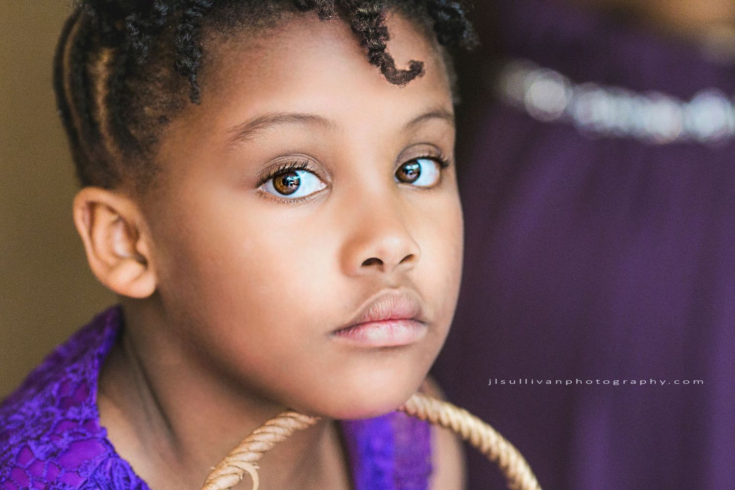 A young person wearing a purple top gazes intently at the camera in a professional portrait setting.