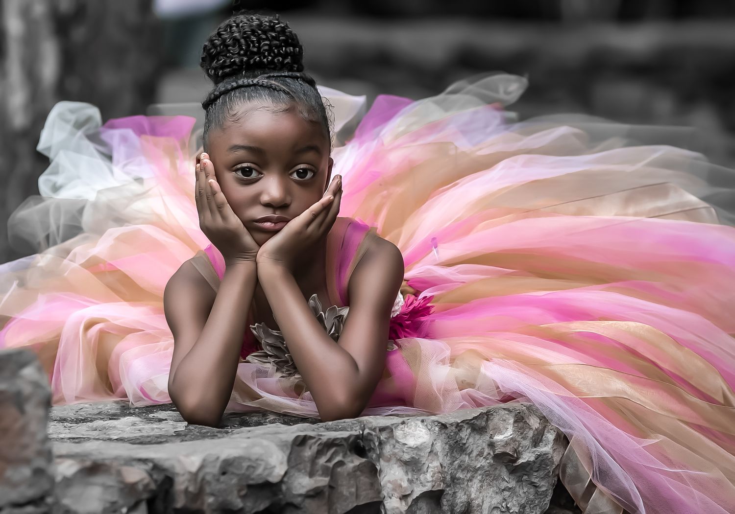 A young dancer in a pink and peach tutu rests head in hands while lying on gray stone.
